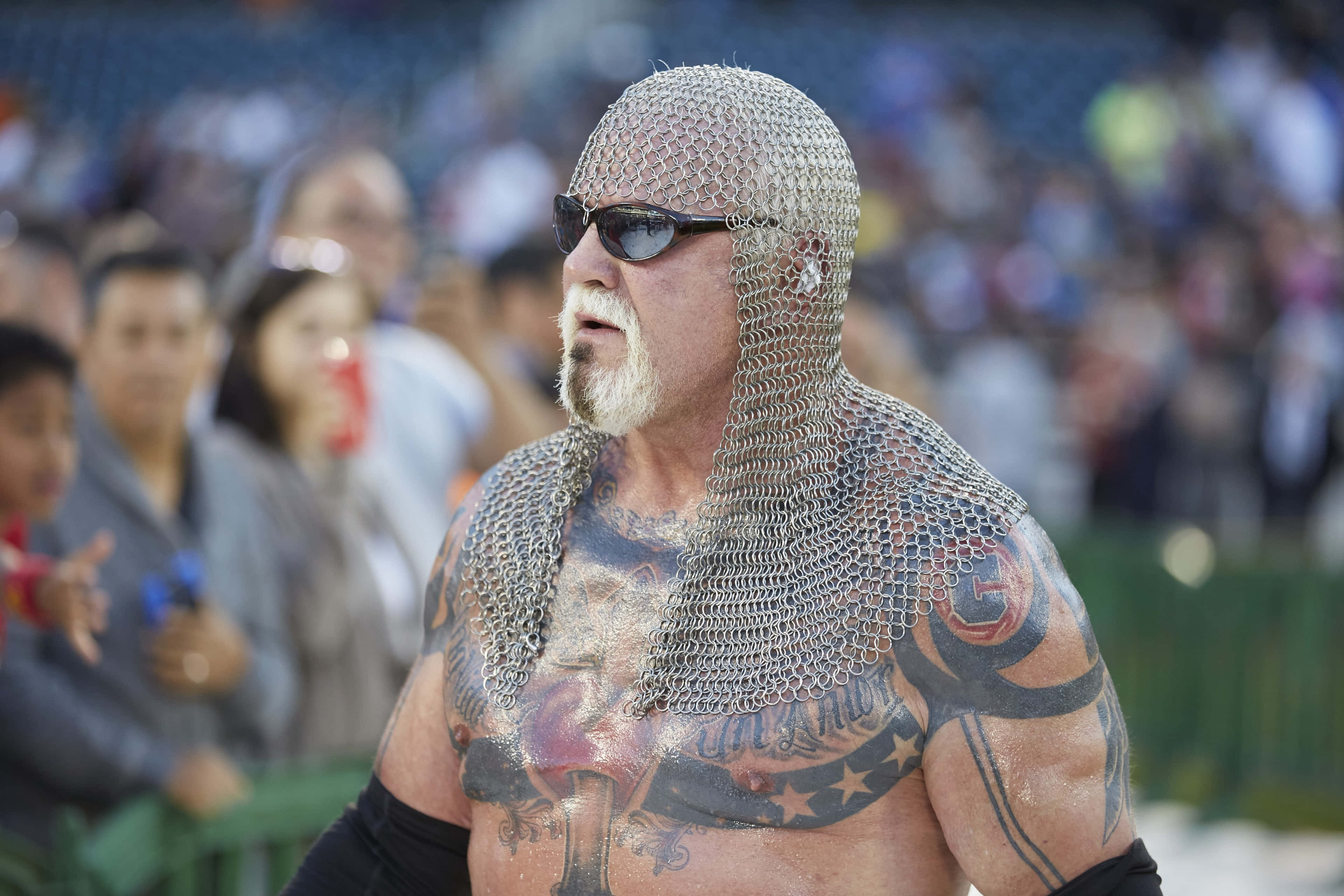 WWE 桌布 壁紙 — 一個有刺青的肌肉男戴著鎖子甲頭罩和太陽眼鏡，站在體育場的人群中。