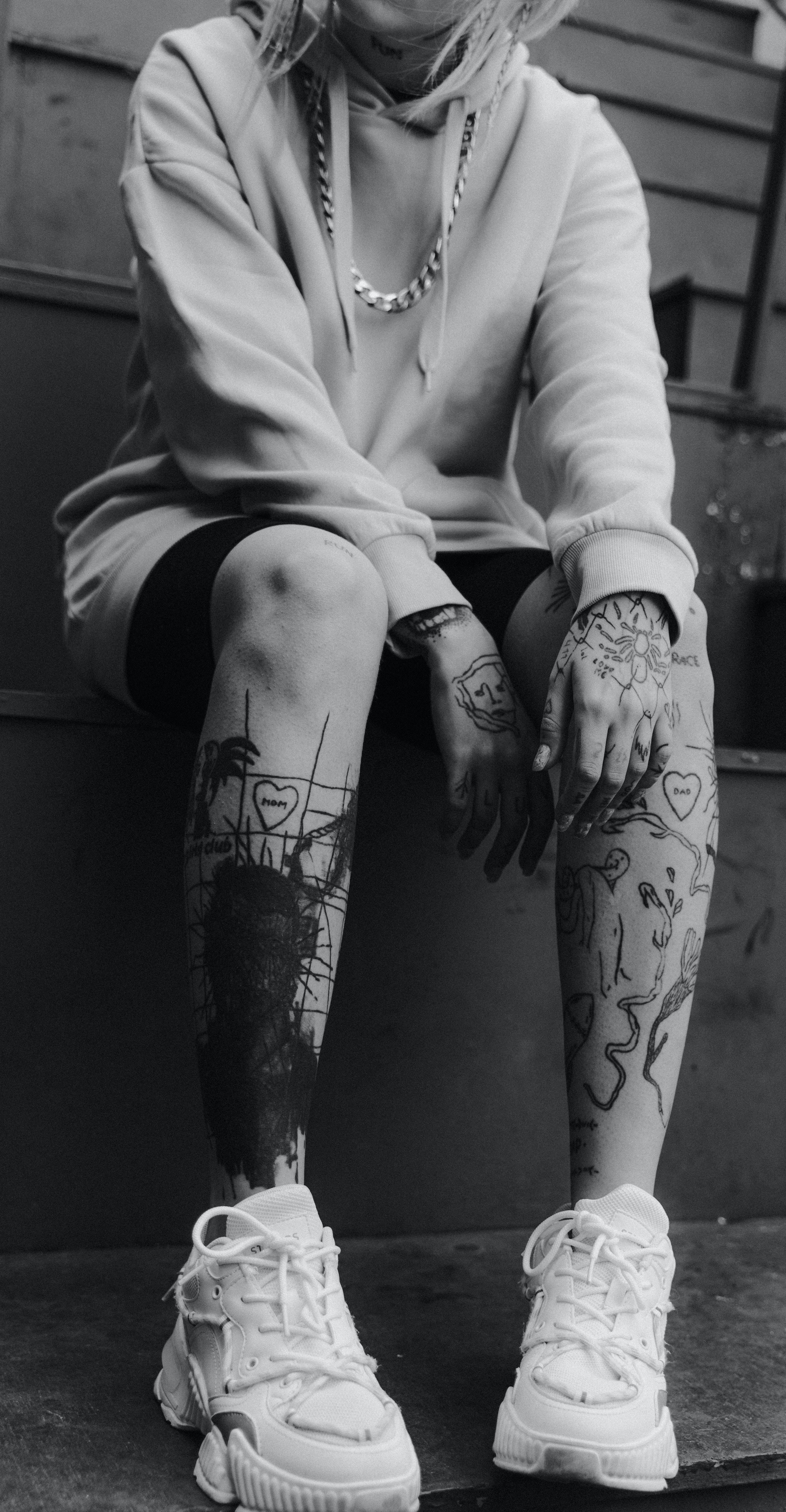 Tattoo 桌布 壁紙 — 一個有大量刺青的人盤腿而坐，穿著連帽衫和厚底運動鞋，黑白風格。