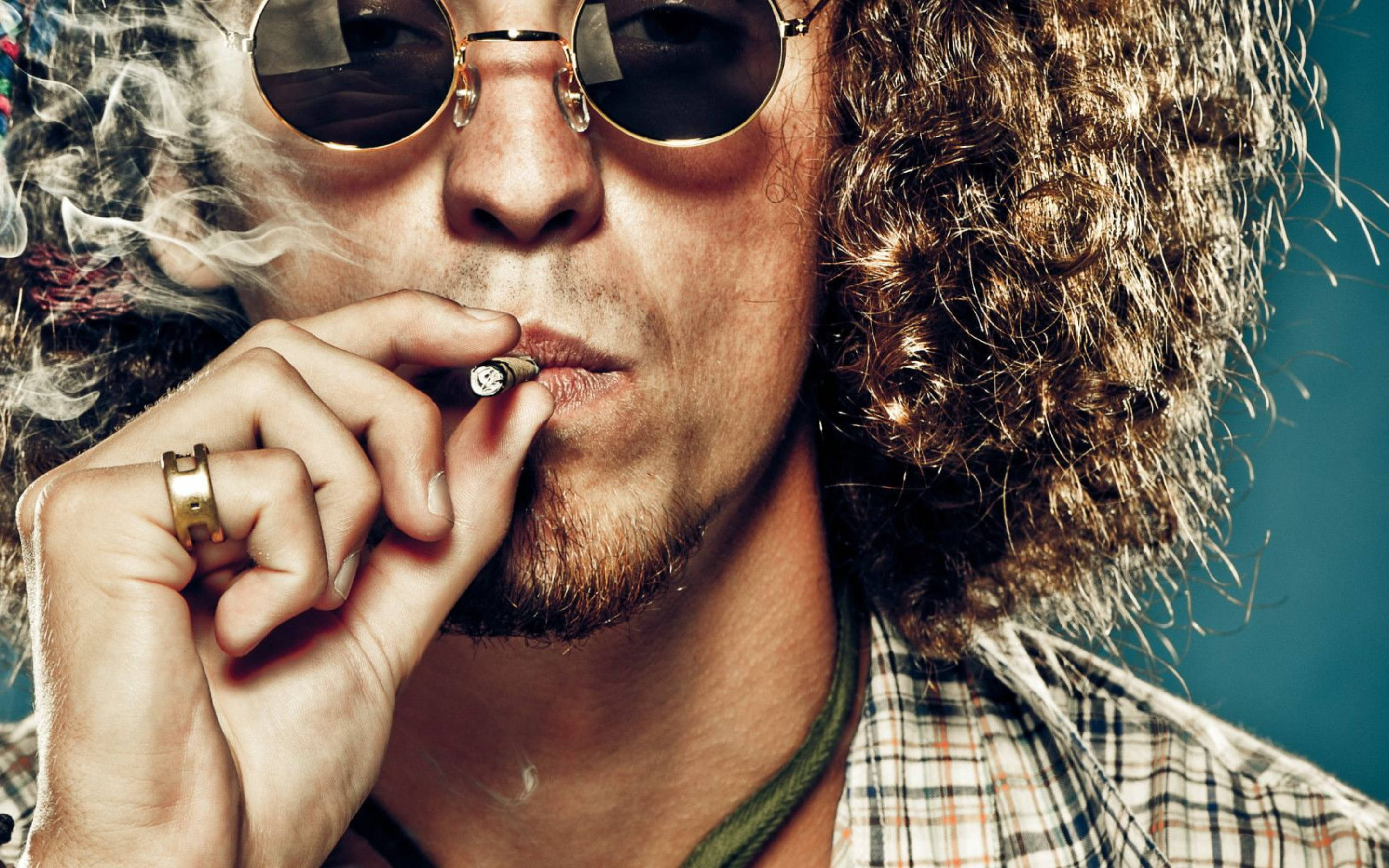 吸大麻 桌布 壁紙 — 一個有捲髮和圓形太陽眼鏡的男人，在嘴唇附近拿著香煙呼出煙霧。