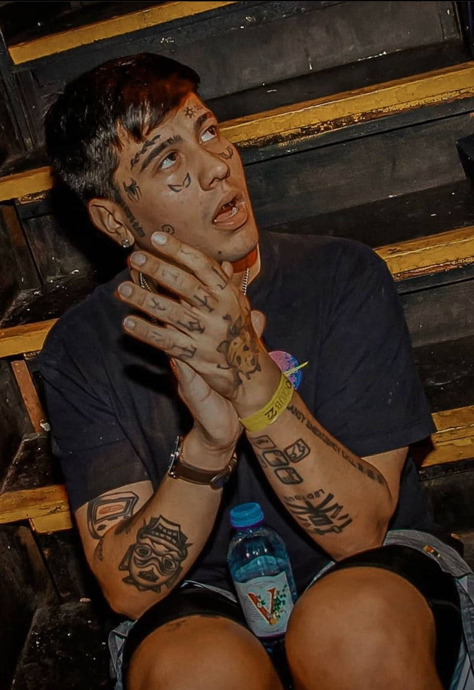 Tattoo 桌布 壁紙 — 一個有星星和骷髏臉部刺青的男人坐在木製看台上，將手放在臉附近。