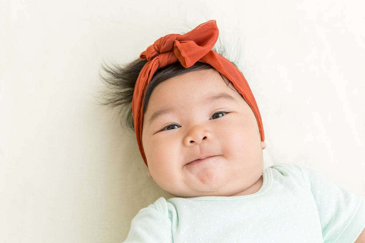 Baby Girl 桌布 壁紙 — 一個有深色眼睛的胖乎乎嬰兒，戴著鏽色蝴蝶結頭帶，在純白色背景前甜美微笑。