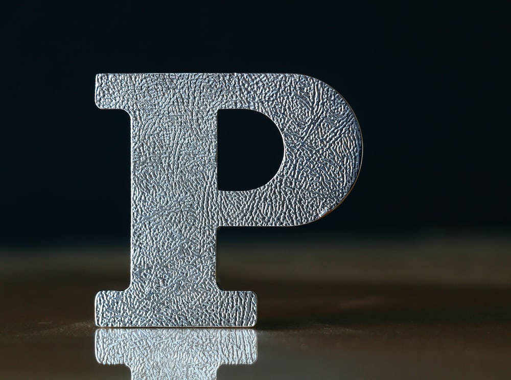 字母P 桌布 壁紙 — 一個有紋理的銀色字母P豎立在反射表面上，背景為深色。
