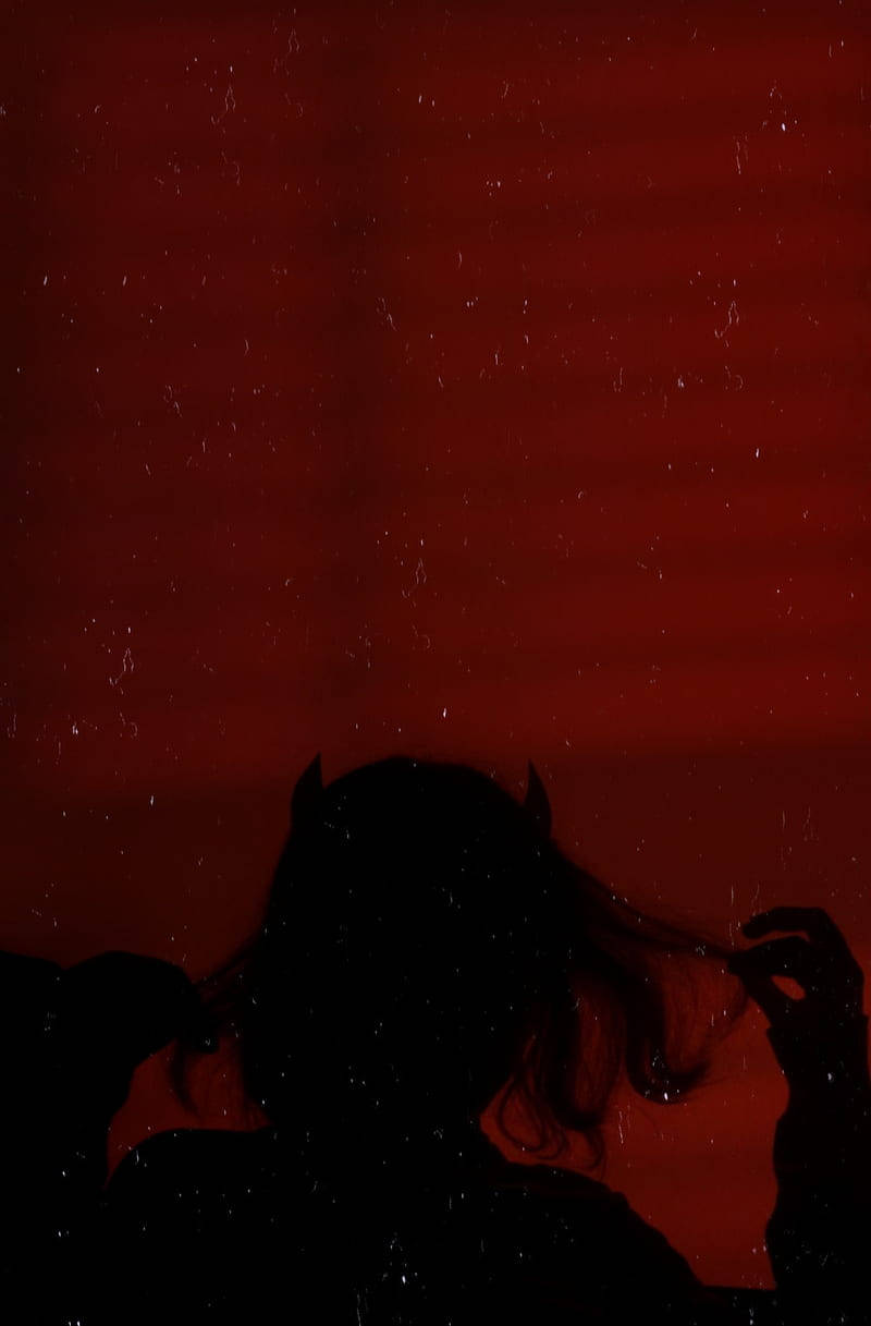 Sad Demon Girl 桌布 壁紙 — 一個有角、頭髮飄逸的人物，在深紅色帶有細微斑點的紋理背景上的黑色剪影。