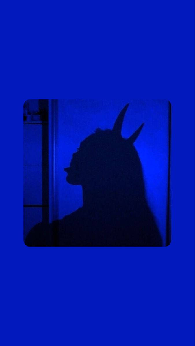 Sad Demon Girl 桌布 壁紙 — 一個有角人物的側面黑色剪影，投射在昏暗房間中一面鮮豔的藍色牆上。