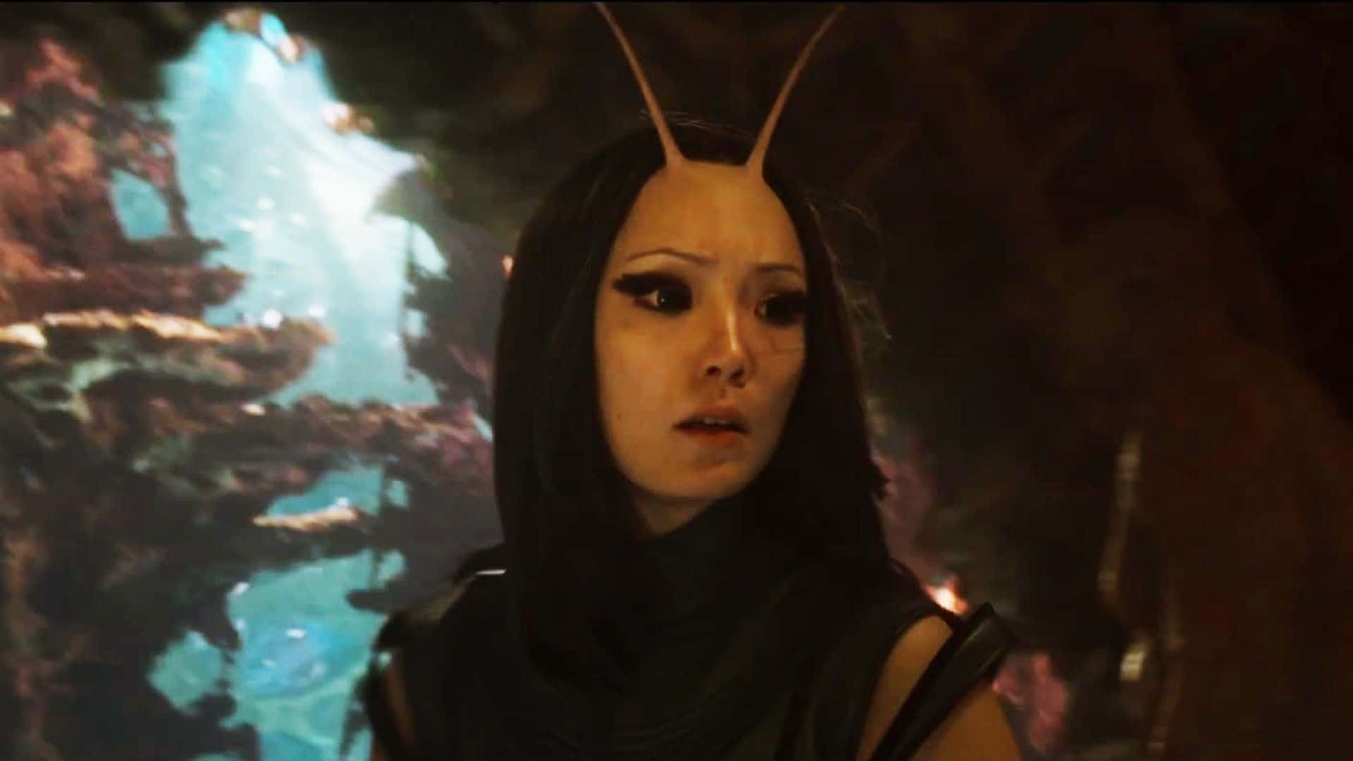 Guardians Of The Galaxy 2 桌布 壁紙 — 一個有觸角的女性外星人在後面有發光藍水的昏暗洞穴中專注地凝視。