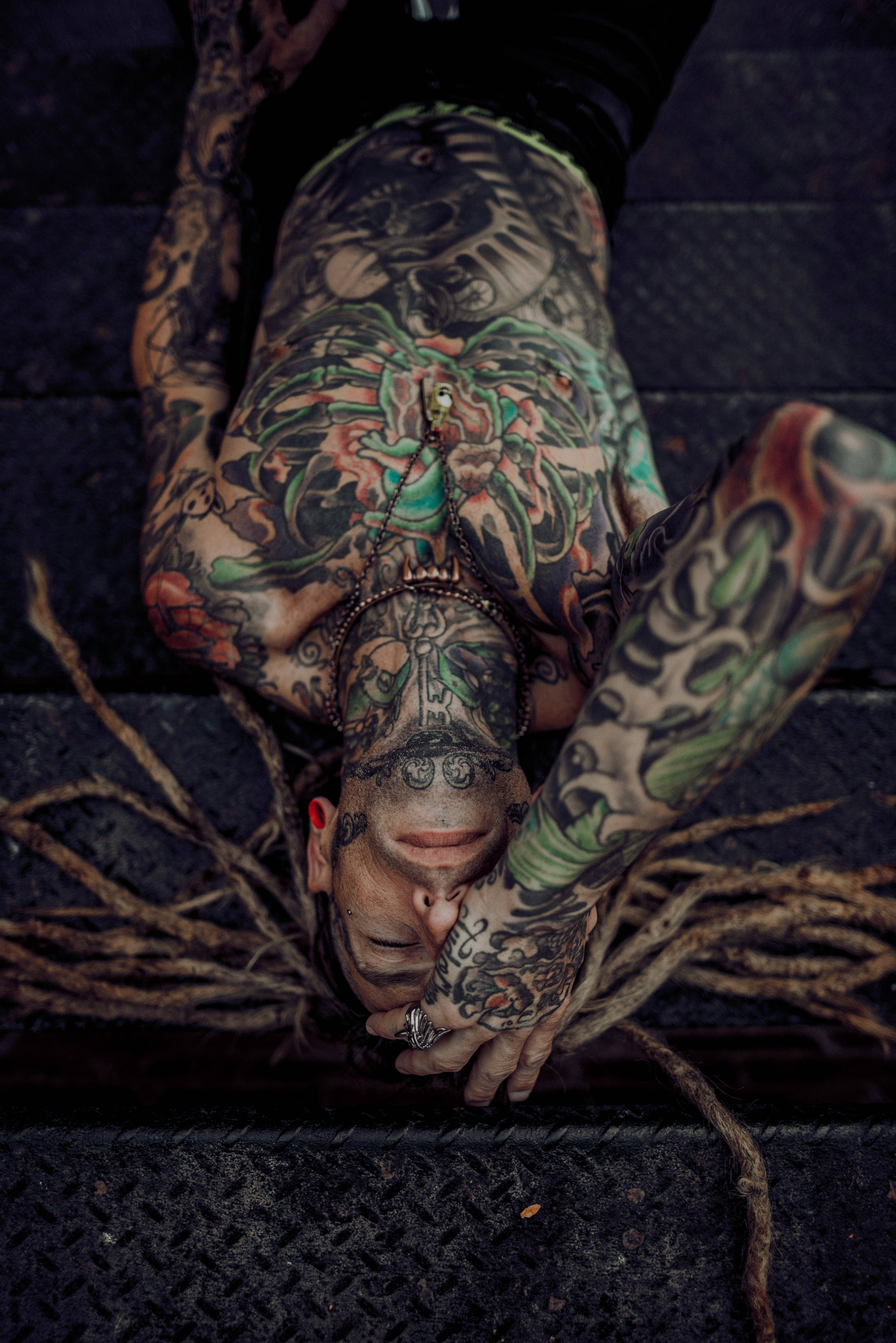 Tattoo 桌布 壁紙 — 一個有辮子刺青的人倒臥在黑暗的階梯上，展示全身複雜多彩的刺青。