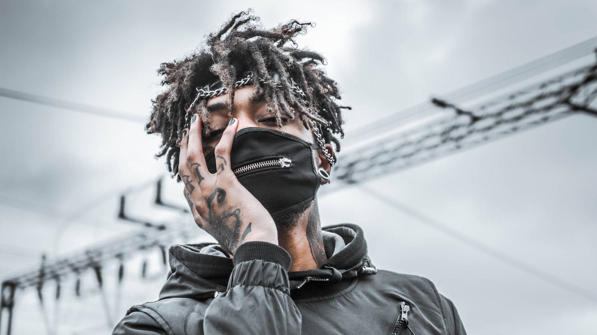 scarlxrd 桌布 壁紙 — 一個有辮子頭和刺青的人用黑色口罩遮住臉，背景是灰色天空和電線。