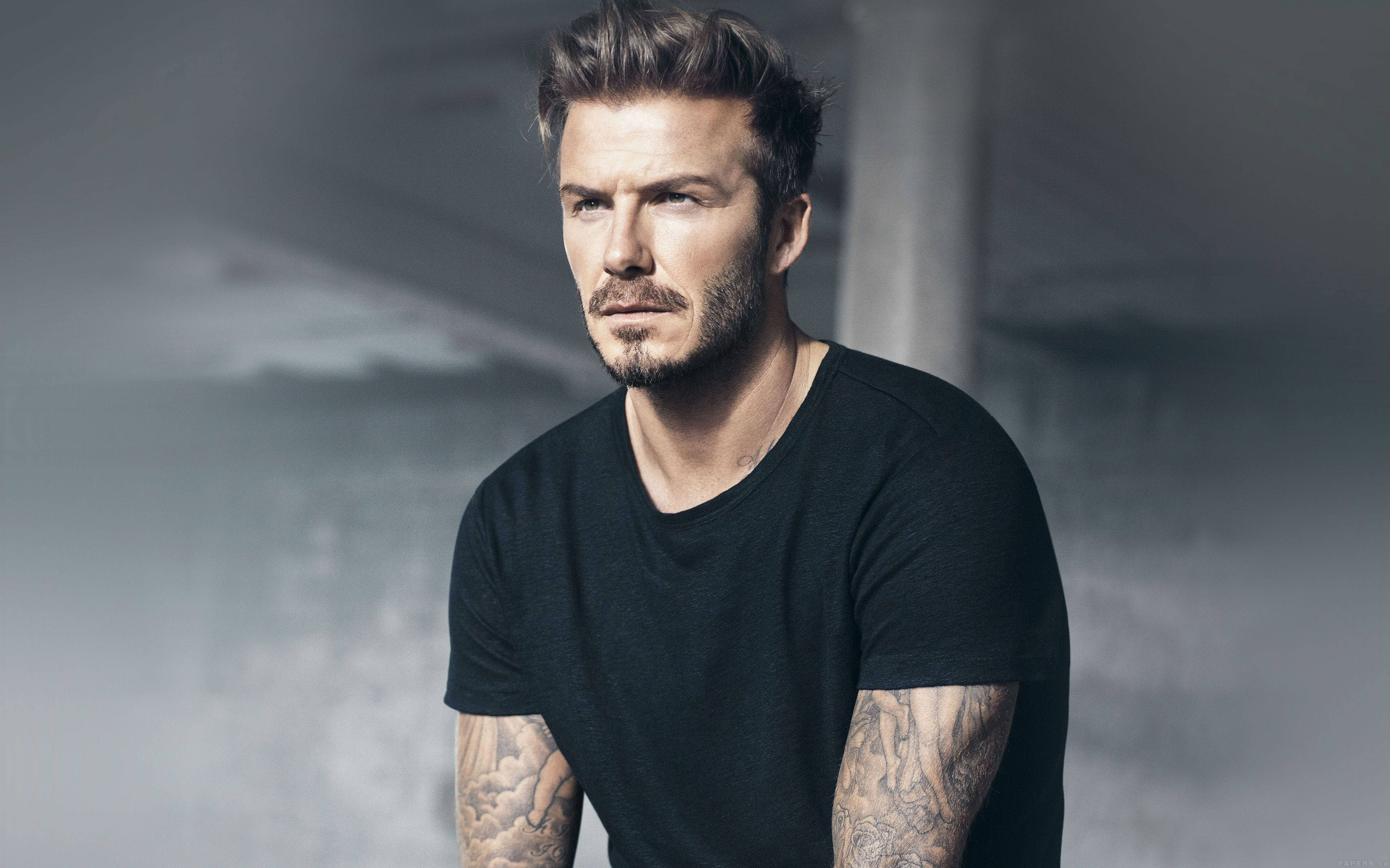 David Beckham 桌布 壁紙 — 一個有造型頭髮和刺青的男人，在柔和的灰色混凝土背景下凝視著。
