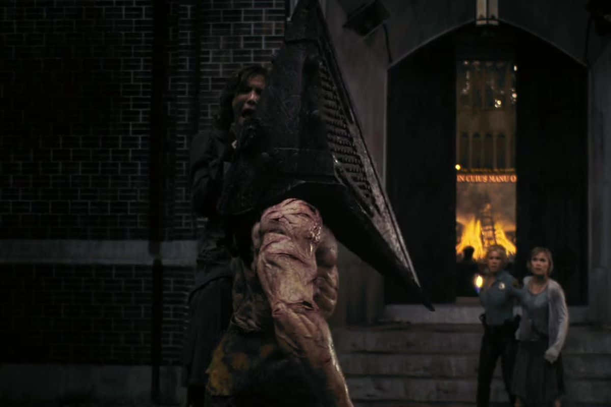 Silent Hill Characters 桌布 壁紙 — 一個有金字塔頭和裸露肉體的怪物般的身影，威脅性地站在燃燒的建築物前，兩個驚恐的女人在黑暗中逃離。