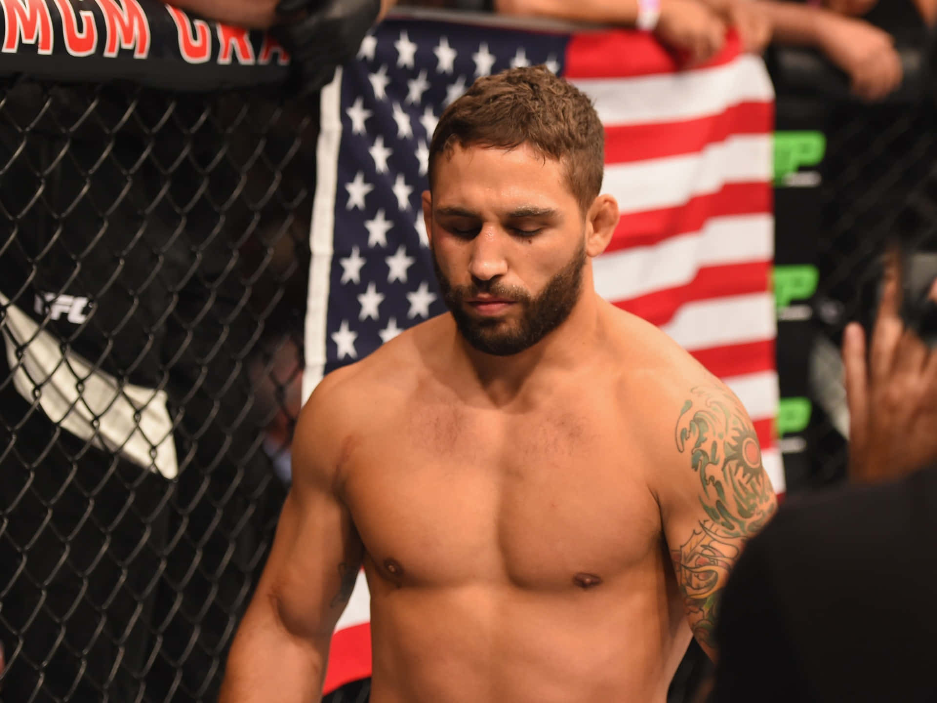 MMA 桌布 壁紙 — 一個有鬍鬚和紋身的肌肉戰士站在UFC八角籠內，身後有美國國旗。