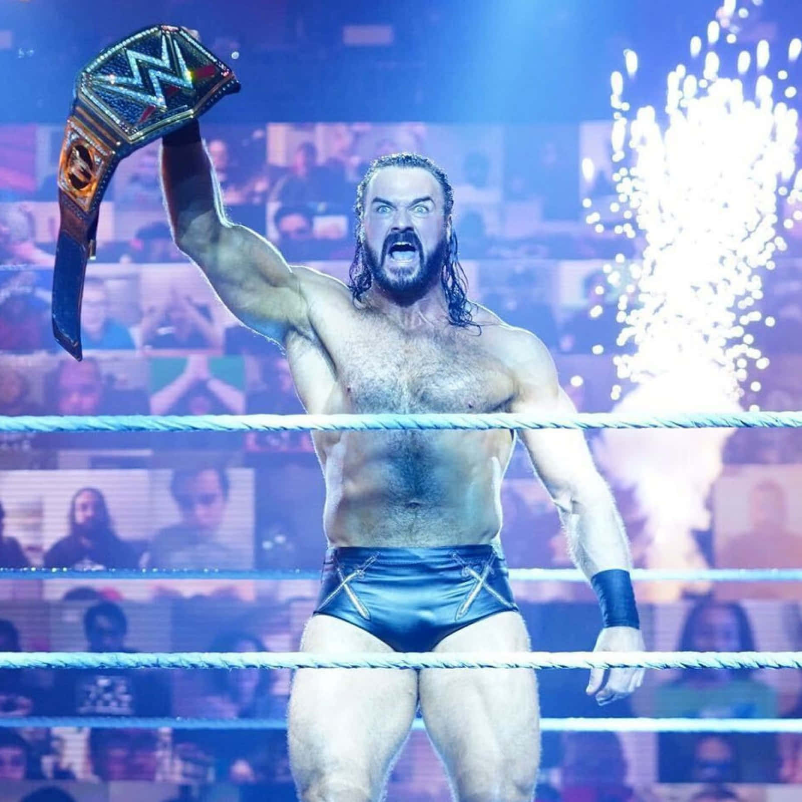 WWE 桌布 壁紙 — 一個有鬍鬚的肌肉發達摔角手在擂台上高舉冠軍腰帶，勝利咆哮，背後煙火爆炸。