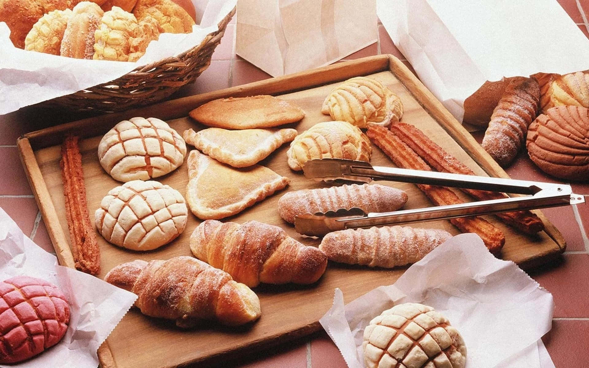 Bakery 桌布 壁紙 — 一個木托盤上放滿了金黃色的糕點，包括可頌和辮子麵包，整齊地排列在磁磚檯面上。