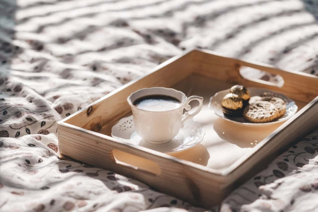 Coffee Cup 桌布 壁紙 — 一個木托盤上放著一個白色咖啡杯和巧克力餅乾，放在圖案床罩上，沐浴在柔和的晨光中。