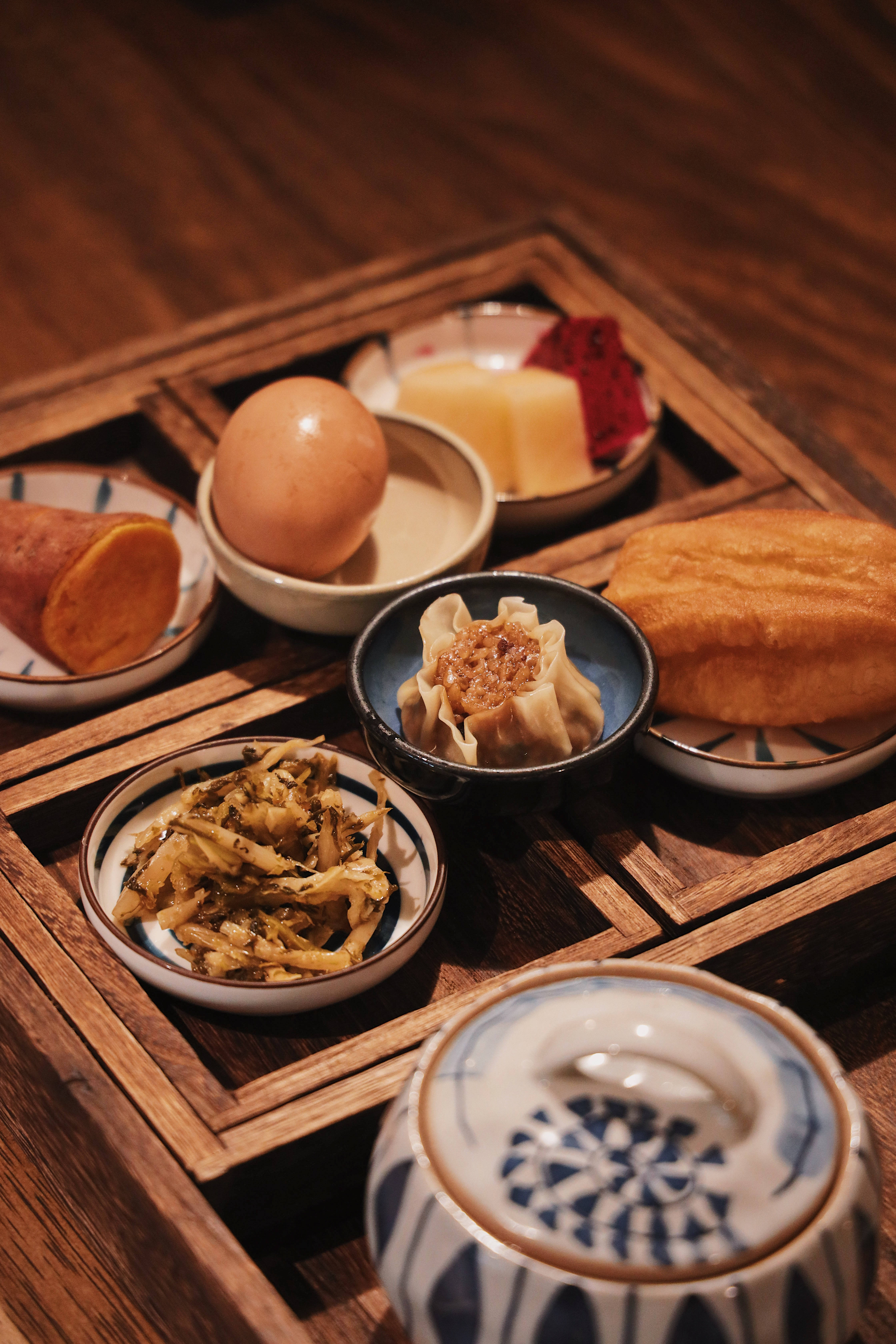 4K 食物 桌布 壁紙 — 一個木托盤在溫暖的環境燈光下盛放著各種傳統亞洲早餐食品，如水餃、雞蛋和醃菜。
