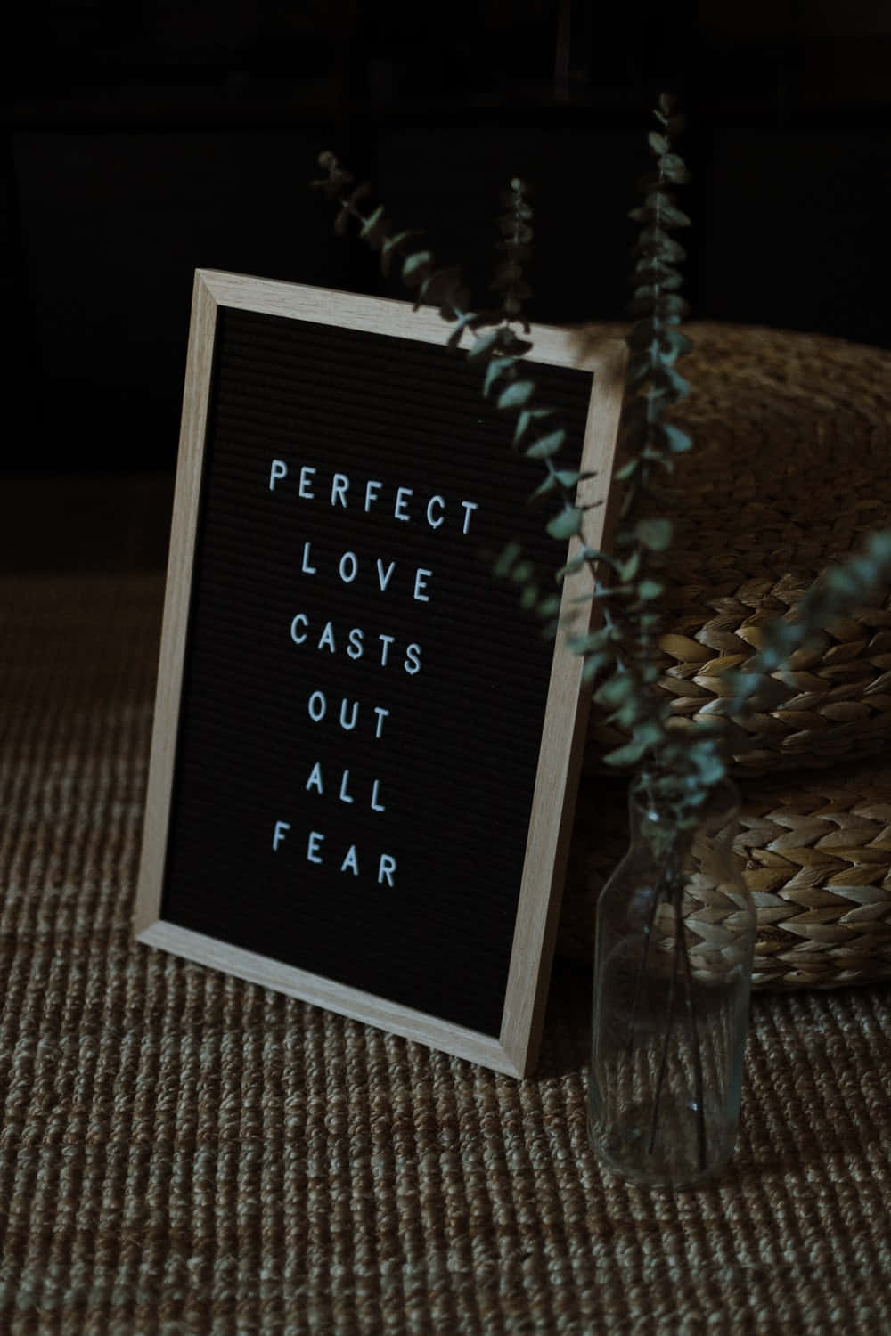 愛情語錄 桌布 壁紙 — 一個木框字母板，上面用白色字母顯示「PERFECT LOVE CASTS OUT ALL FEAR」，旁邊有一個帶有尤加利葉的玻璃花瓶和一個放在有紋理地毯上的編織籃。