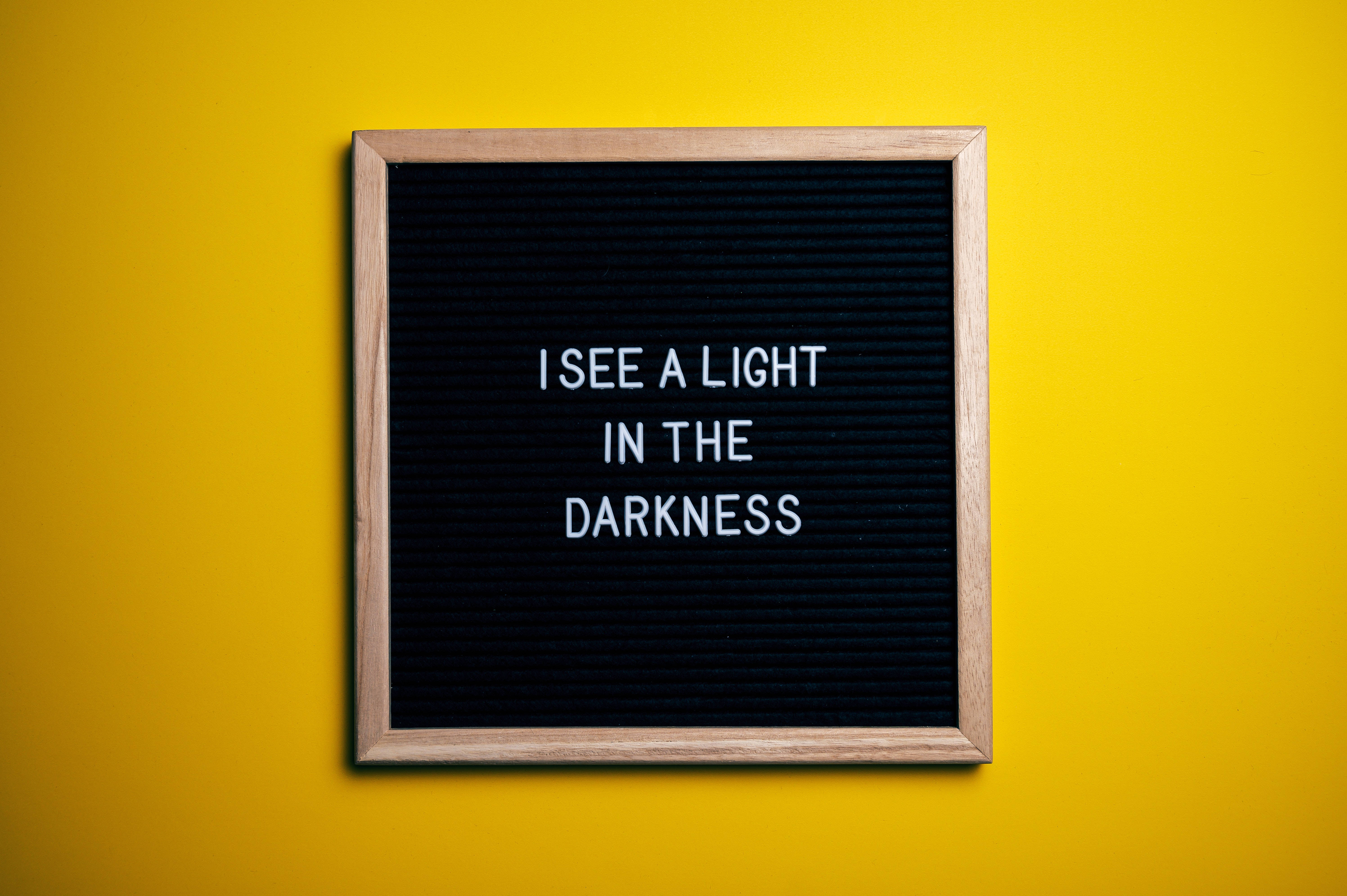 Positive 桌布 壁紙 — 一個木框字母板，在鮮黃色背景上用白色字母拼出「I SEE A LIGHT IN THE DARKNESS」。