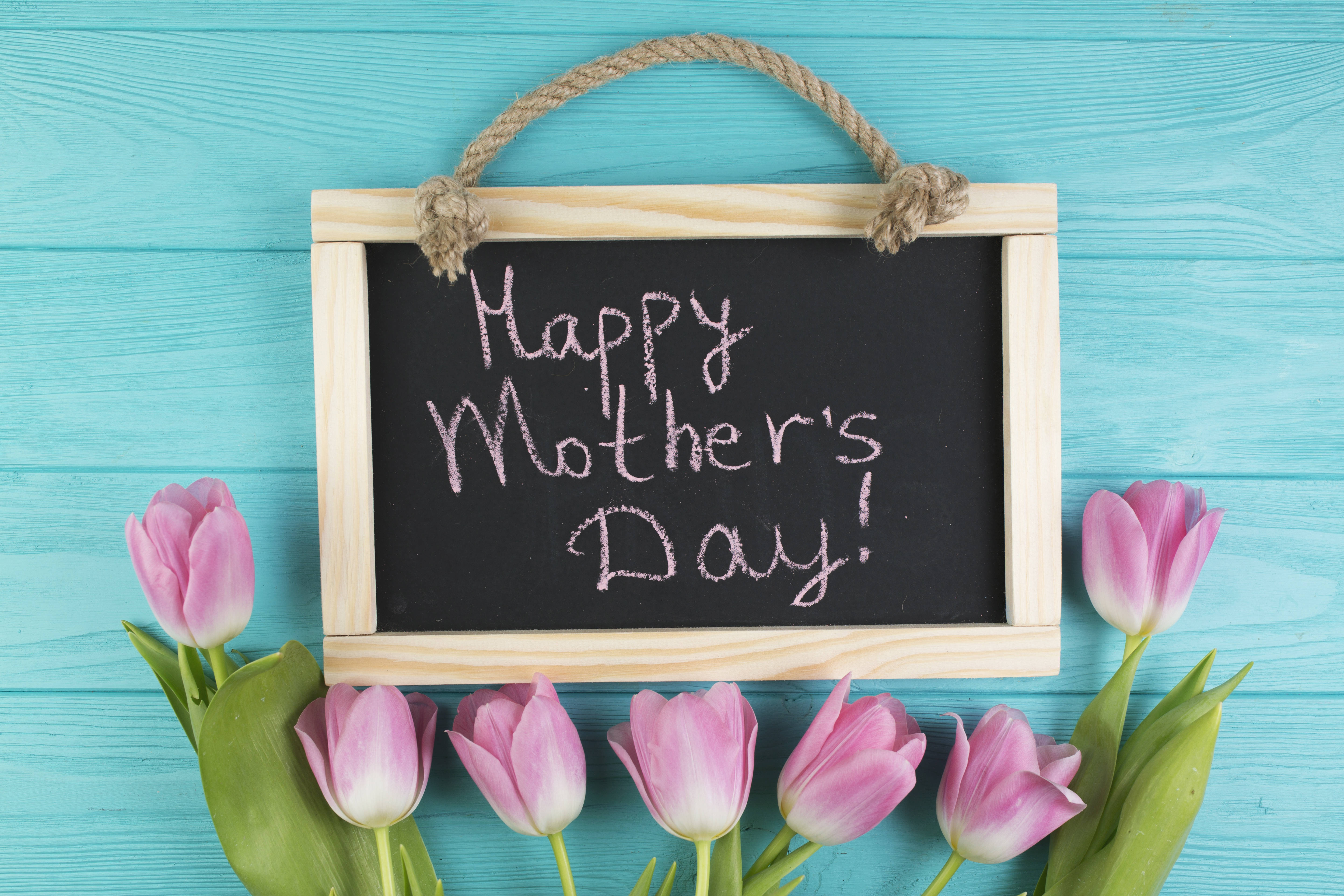 Happy Mothers Day 桌布 壁紙 — 一個木框黑板，上面寫著「Happy Mother's Day!」，周圍環繞著粉紅色鬱金香，背景是藍綠色的木頭。