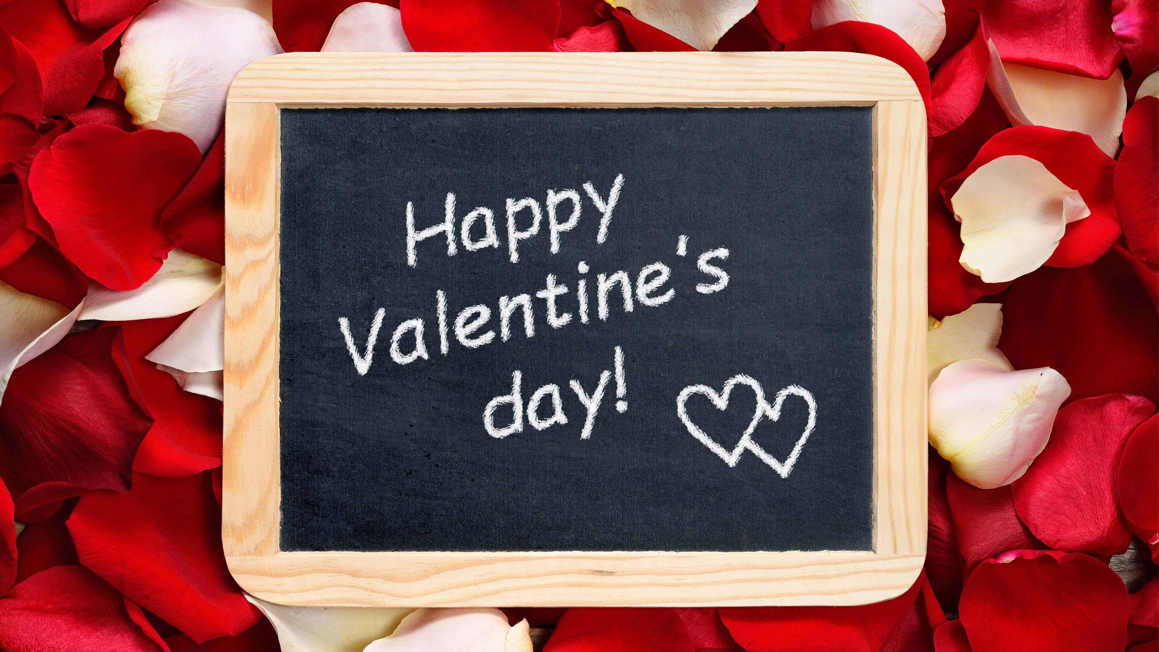 Happy Valentines Day 桌布 壁紙 — 一個木框黑板，用白色粉筆寫上「Happy Valentine's day!」和兩個心形，周圍環繞著紅色和奶油色的玫瑰花瓣。