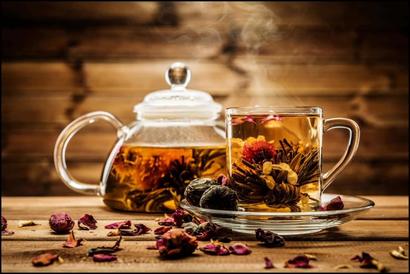 一個木桌上的茶壺，周圍有花朵與茶葉 壁紙