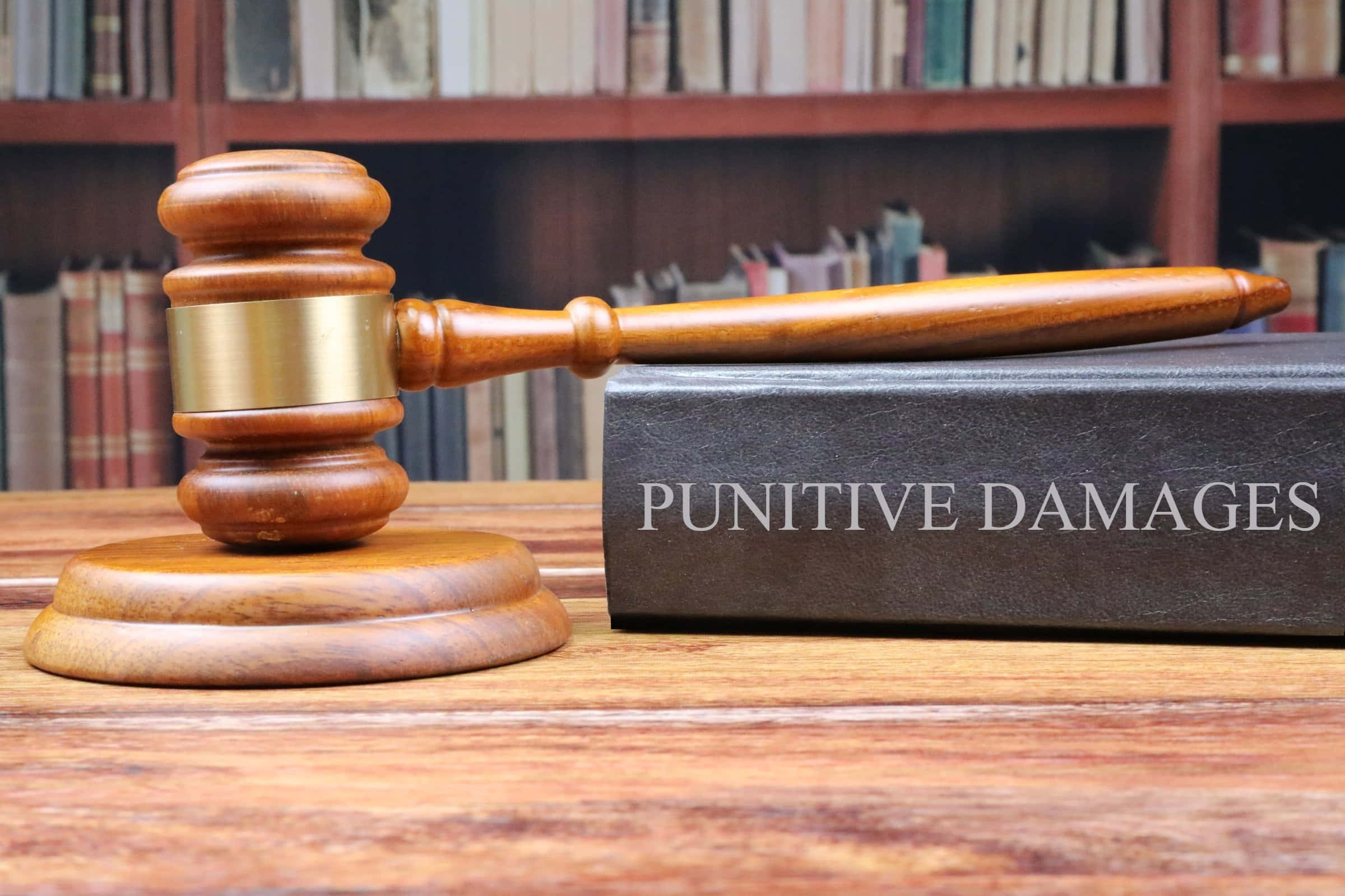 風景 桌布 壁紙 — 一個木槌放在桌上，旁邊有一本名為 punitive damages 的書，背景是書架。