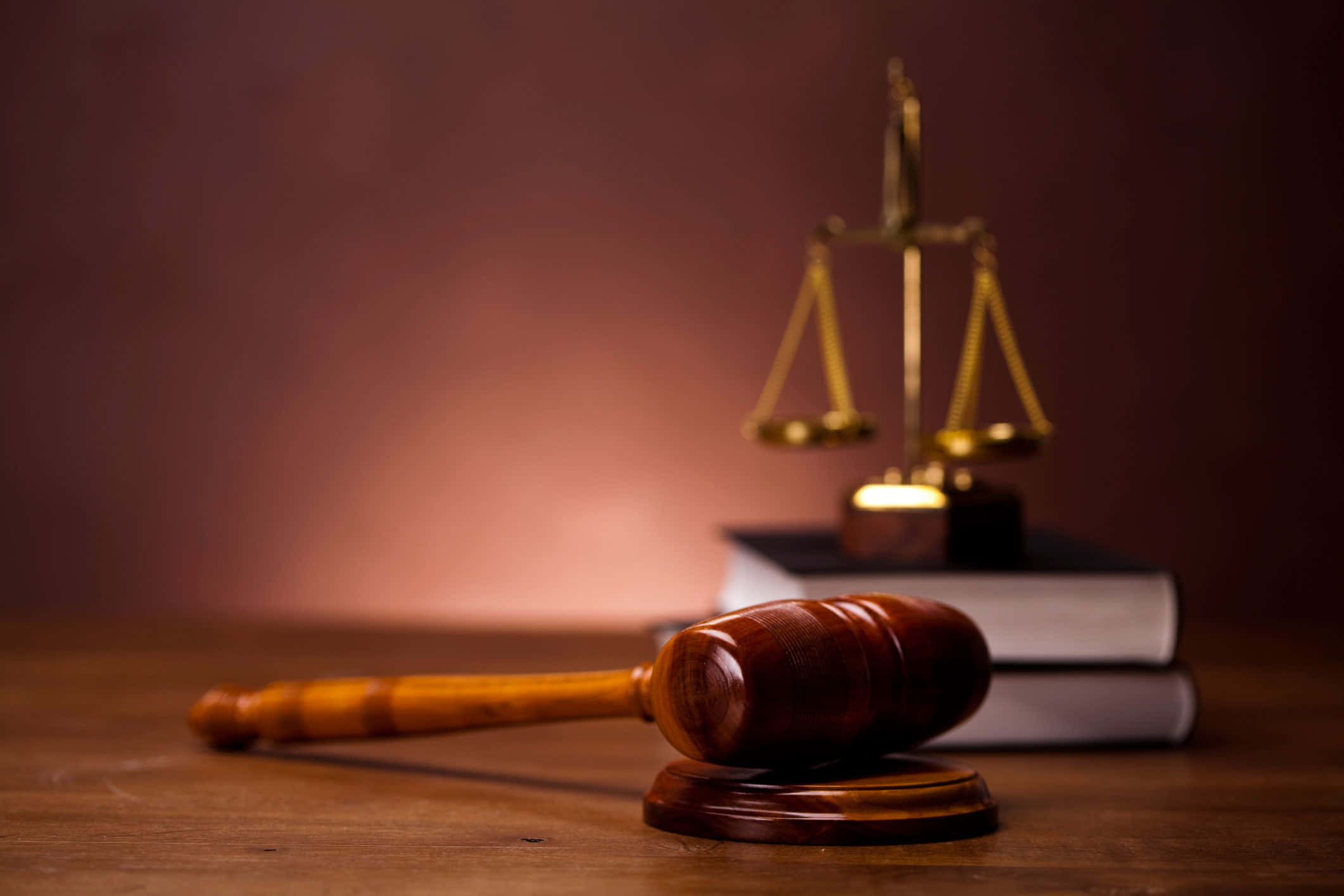 Law 桌布 壁紙 — 一個木槌放在桌子上，旁邊是金色正義天秤，放在法律書上，在溫暖的燈光下。