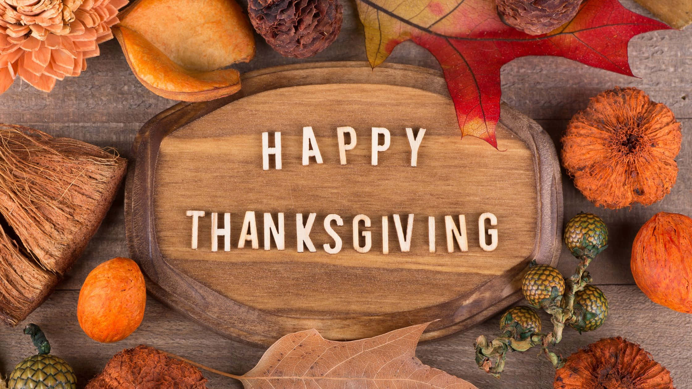 感恩節 桌布 壁紙 — 一個木牌上寫著「HAPPY THANKSGIVING」，周圍環繞著秋葉、松果和葫蘆，放置在質樸的木質表面上。