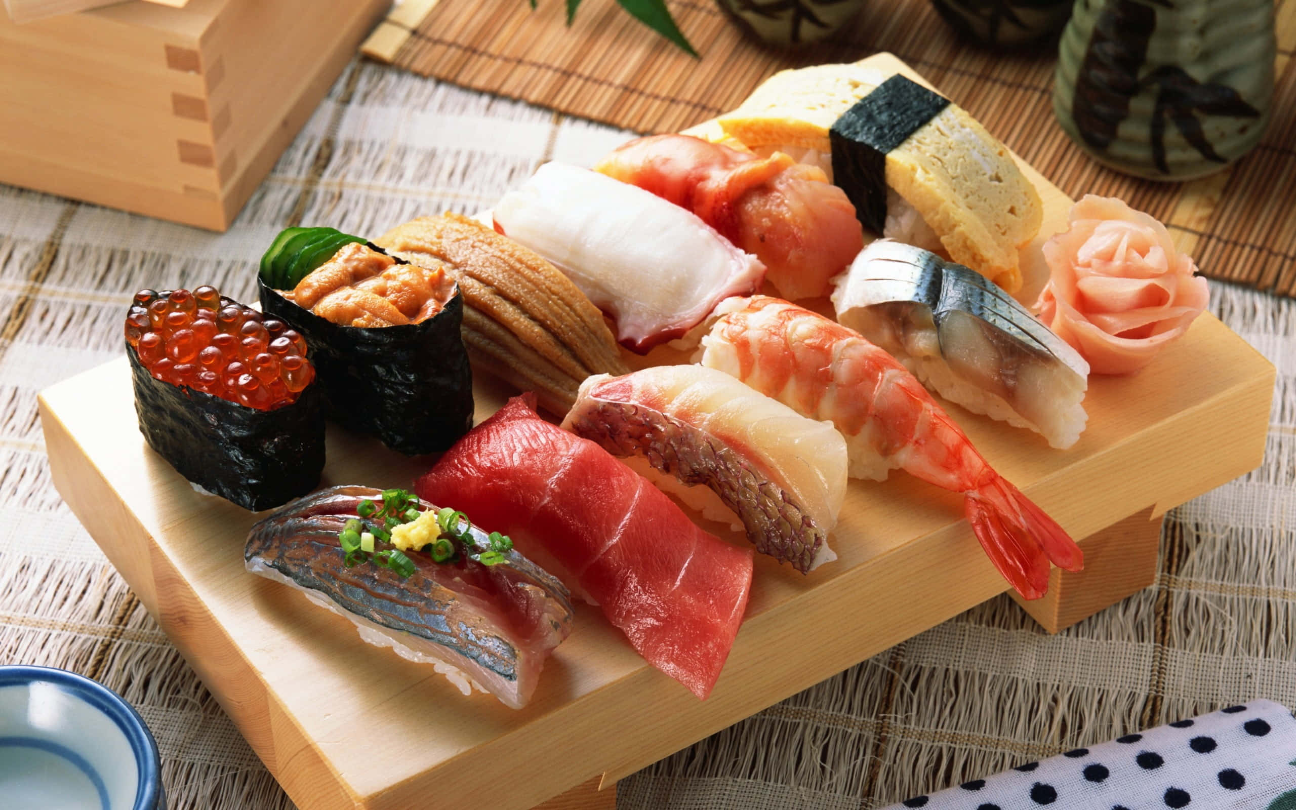 Salmon 桌布 壁紙 — 一個木盤上展示著各種色彩繽紛的壽司，包括鮪魚、蝦和魚卵，擺放在編織墊上。