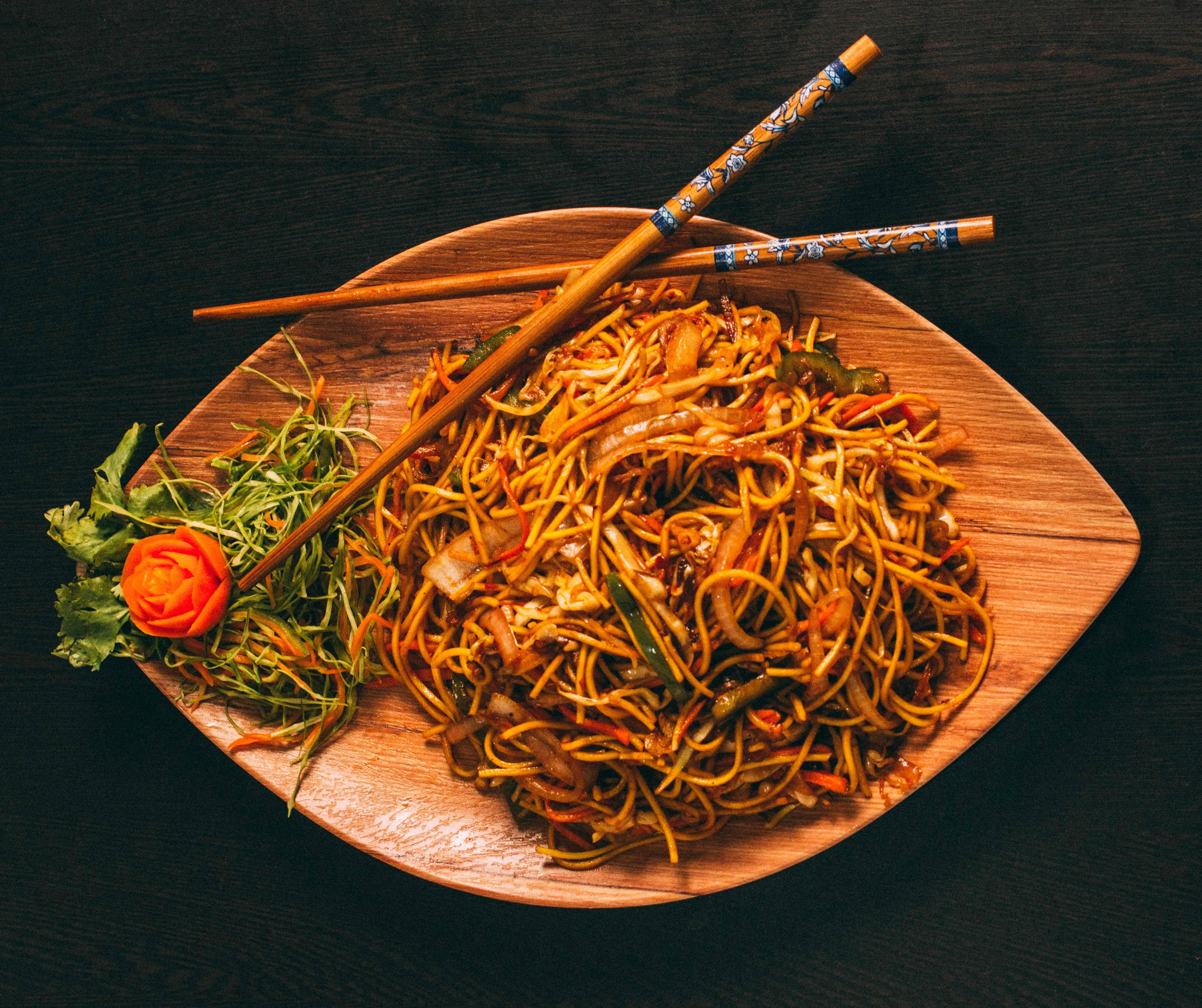 Healthy Food 桌布 壁紙 — 一個木盤上盛載著冒煙的炒麵，上面放著筷子，旁邊有雕刻的胡蘿蔔玫瑰和新鮮蔬菜。