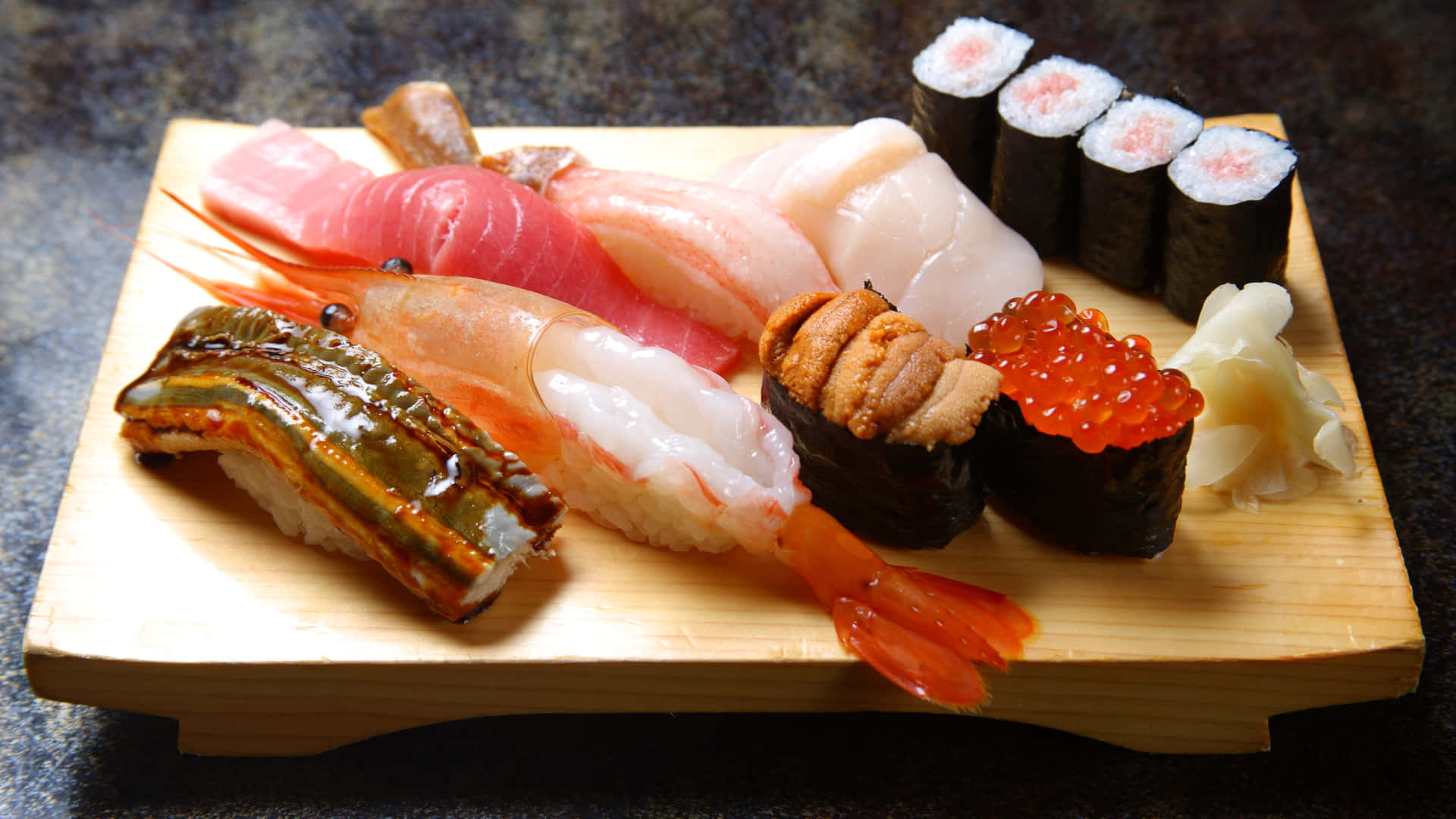 Sushi 桌布 壁紙 — 一個木盤在溫暖燈光下展示各種新鮮壽司，包括鮪魚、蝦、鰻魚和鮭魚卵。
