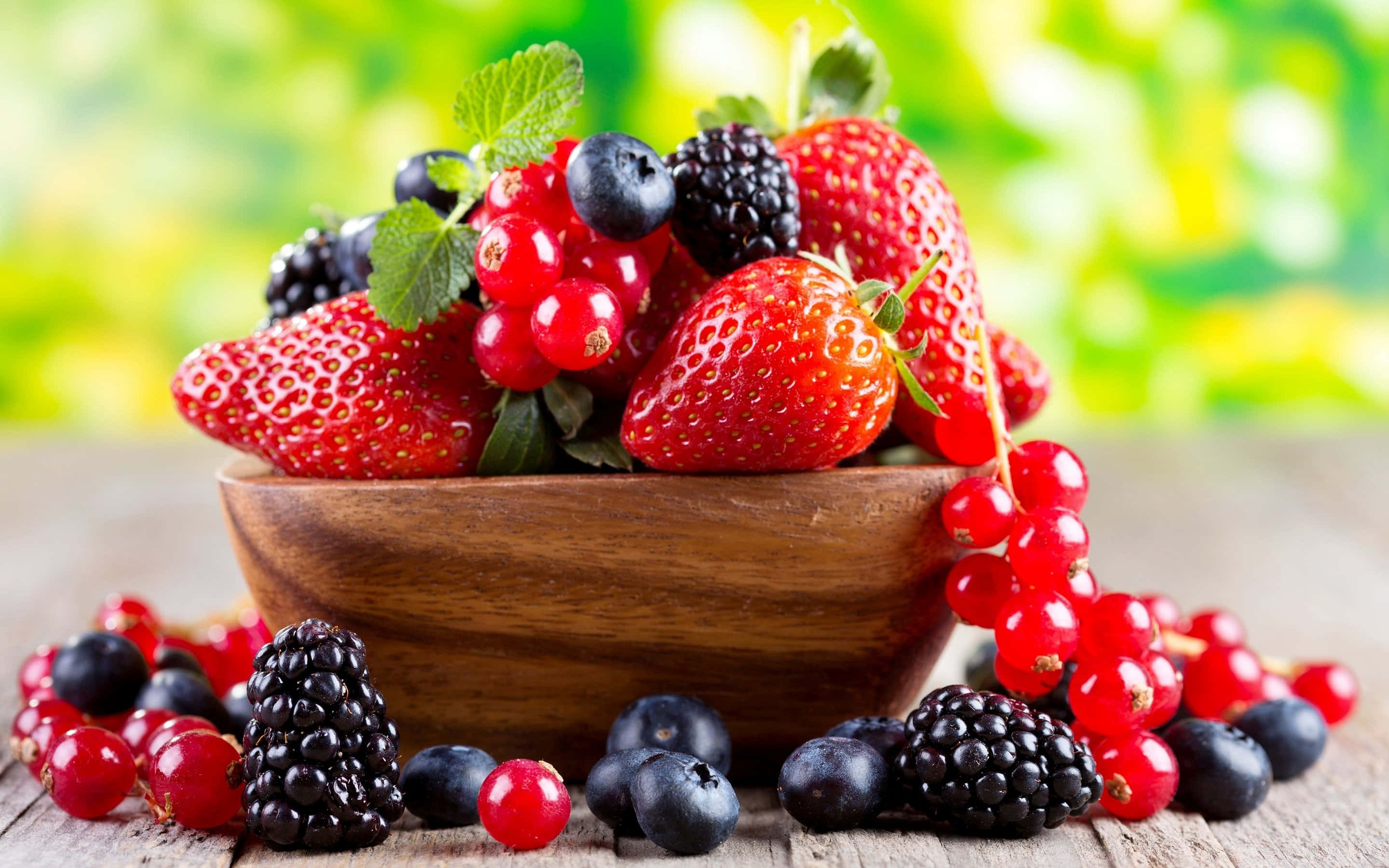 Raspberry 桌布 壁紙 — 一個木碗盛滿了鮮豔的草莓、黑莓、藍莓和紅醋栗，放在質樸的木桌上。