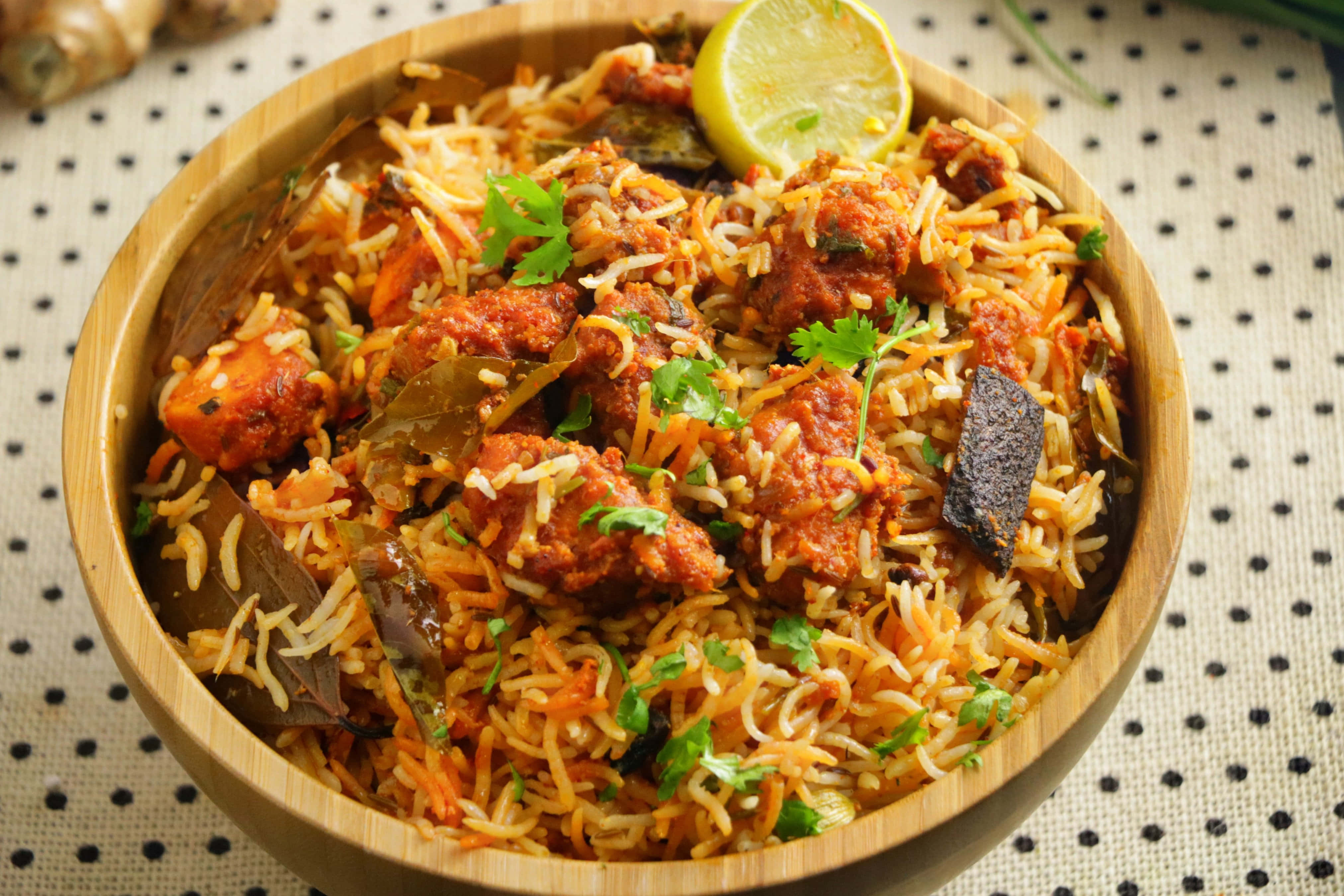 Biryani 桌布 壁紙 — 一個木碗盛滿香氣撲鼻的印度香飯和嫩肉塊，上面點綴著新鮮香菜和萊姆角。