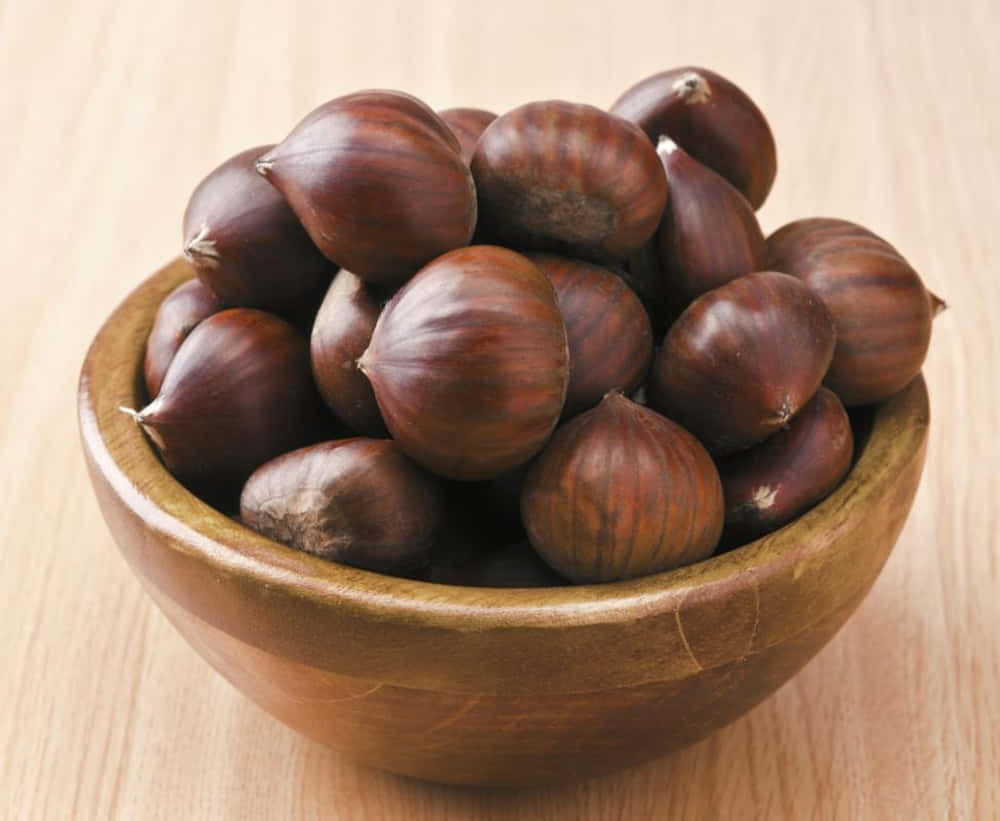 Chestnut 桌布 壁紙 — 一個木碗裝滿了光澤的棕色栗子，放在淺色木質表面上。