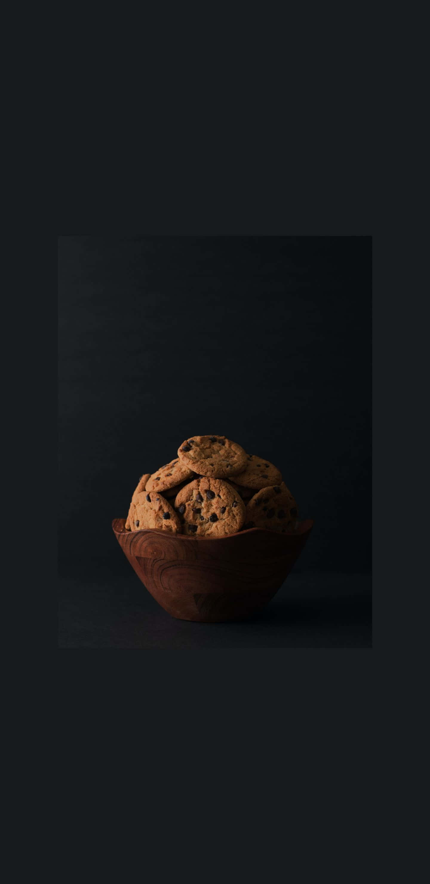 Pastry 桌布 壁紙 — 一個木碗裝滿了巧克力餅乾，置於深黑色背景中央，在柔和的方向性燈光下。