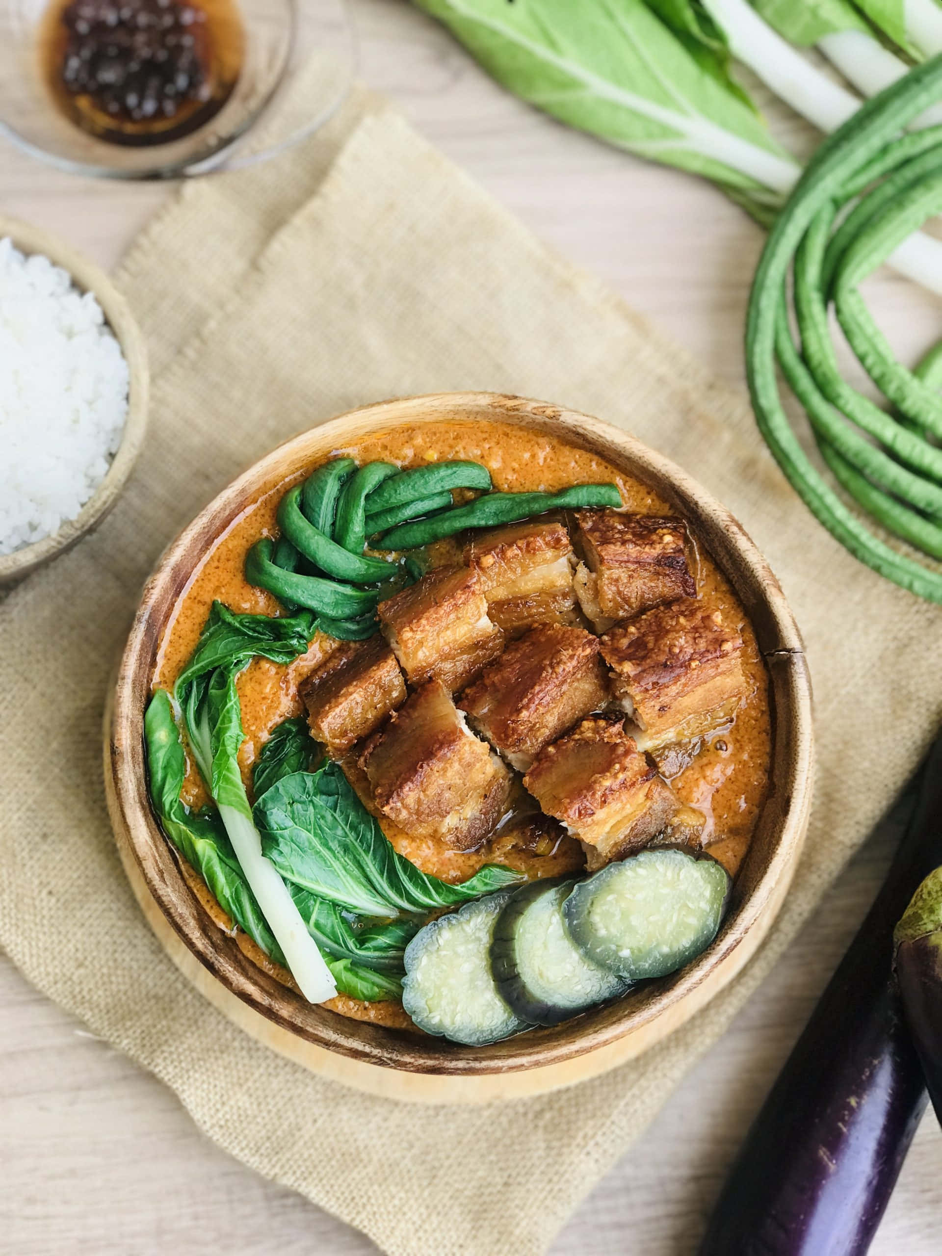meat 桌布 壁紙 — 一個木碗裝滿了豐富的釉面五花肉、鮮綠色的青江菜和黃瓜片，周圍是新鮮蔬菜和米飯，放在一塊質樸的布上。