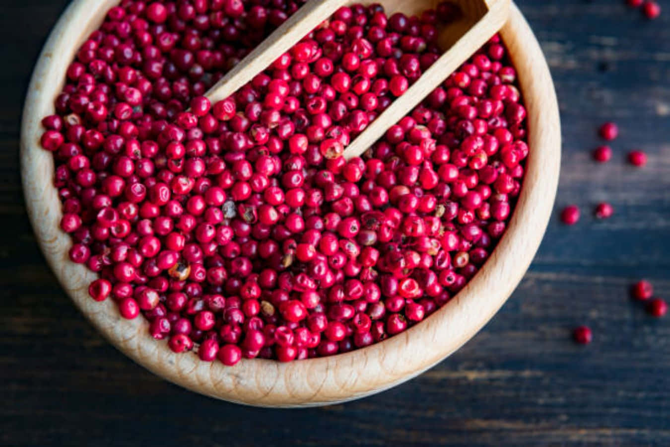 Pink Peppercorn 桌布 壁紙 — 一個木碗裝滿了鮮紅色的胡椒粒，配有一個相配的勺子，放在深色質樸的木質表面上。