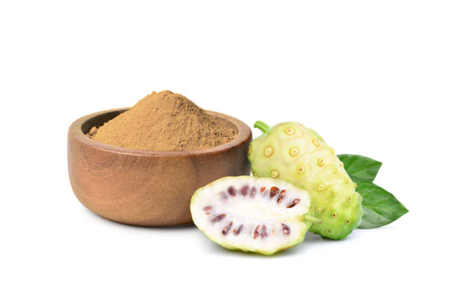 Fruits 桌布 壁紙 — 一個木碗裝滿棕色諾麗果粉，旁邊放著一個完整和切片的綠色諾麗果，連同葉子，在白色背景上。