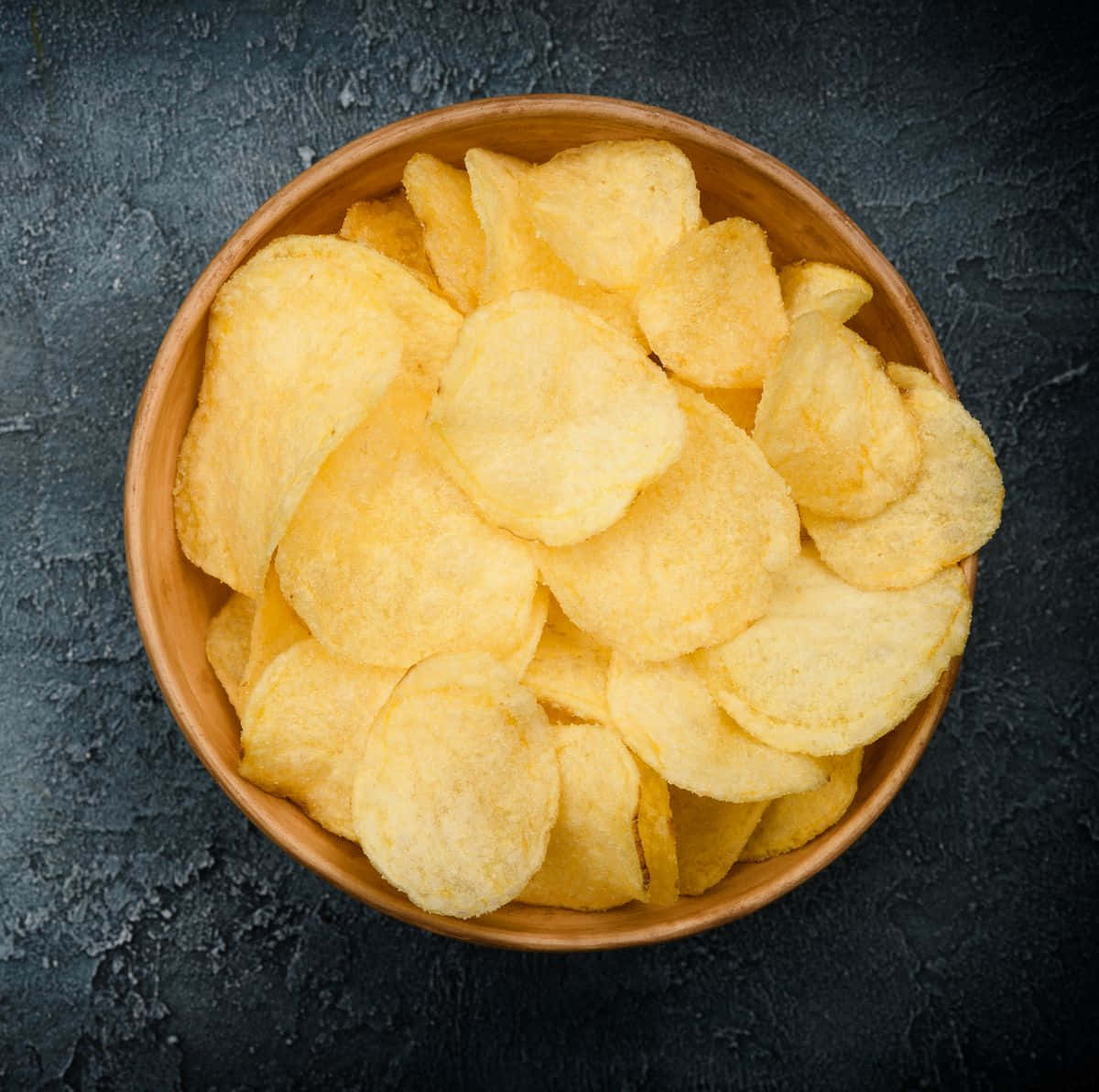 Snacks 桌布 壁紙 — 一個木碗裝滿金黃色薯片，放在深色紋理表面上。