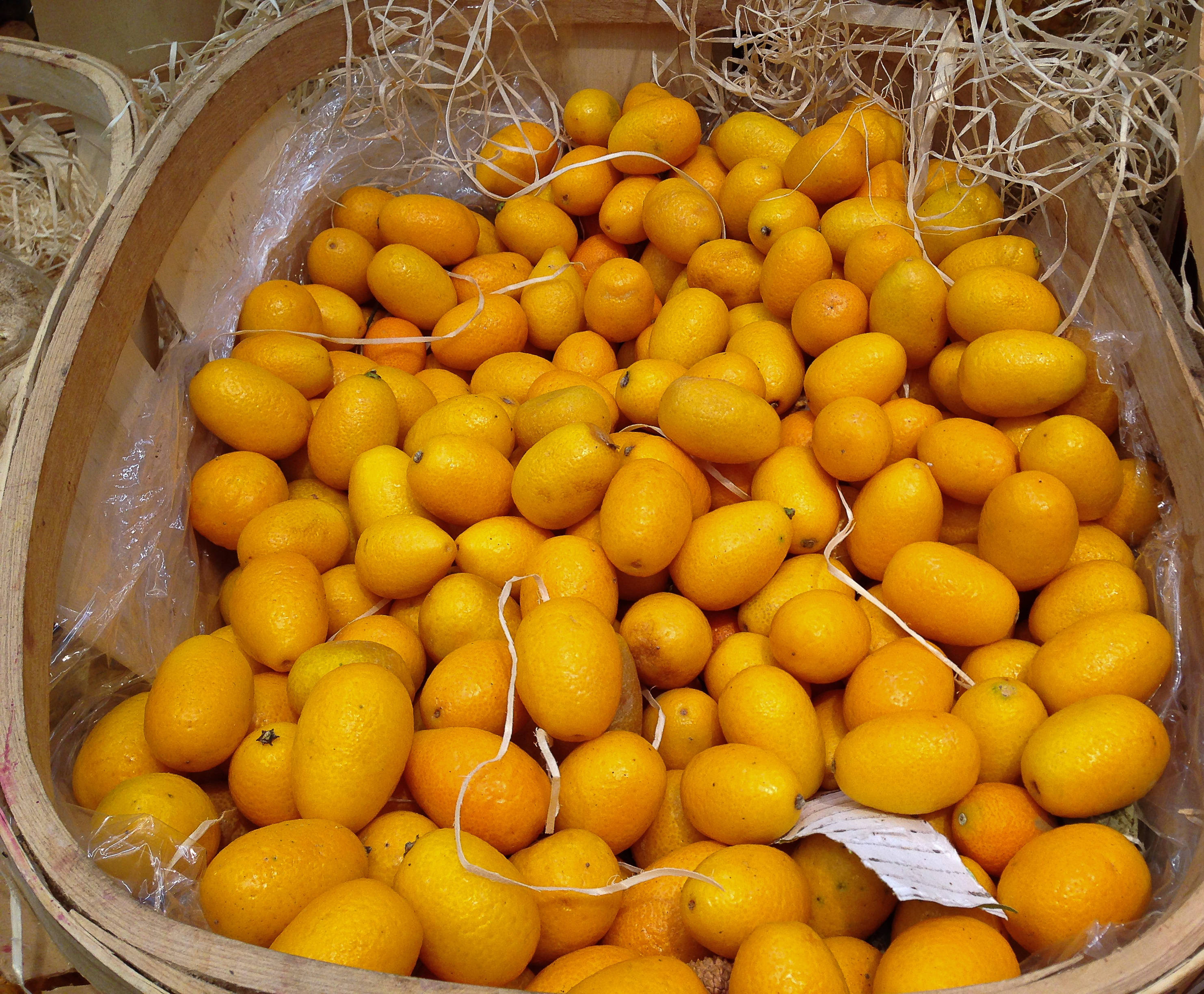 Kumquat 桌布 壁紙 — 一個木籃子裝滿了鮮黃色的金桔，放在稻草和保鮮膜中。