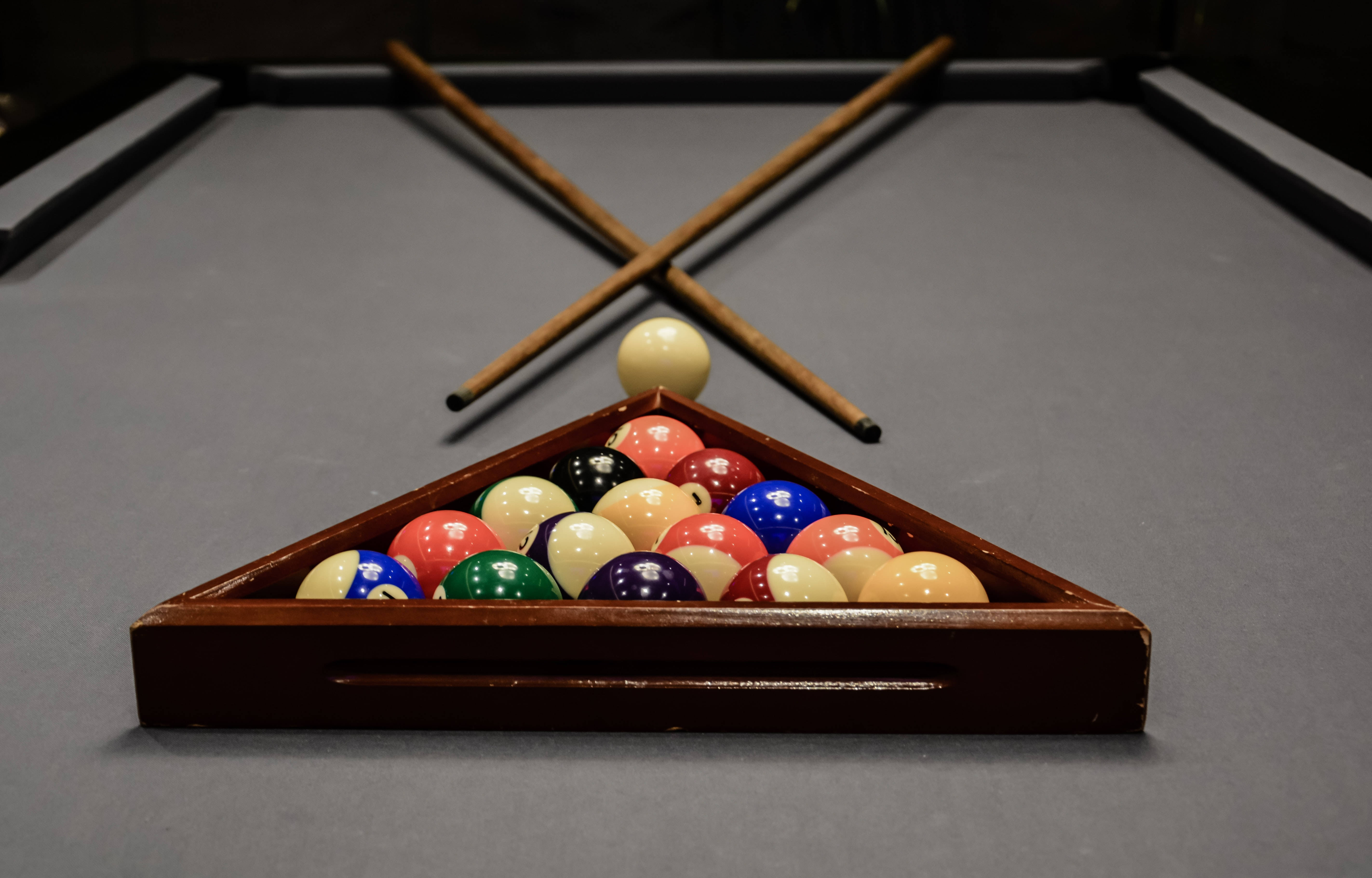 Snooker 桌布 壁紙 — 一個木製三角形架的特寫，上面放著色彩繽紛的撞球，後面有兩支交叉的球桿擱在灰色絨面撞球檯上。