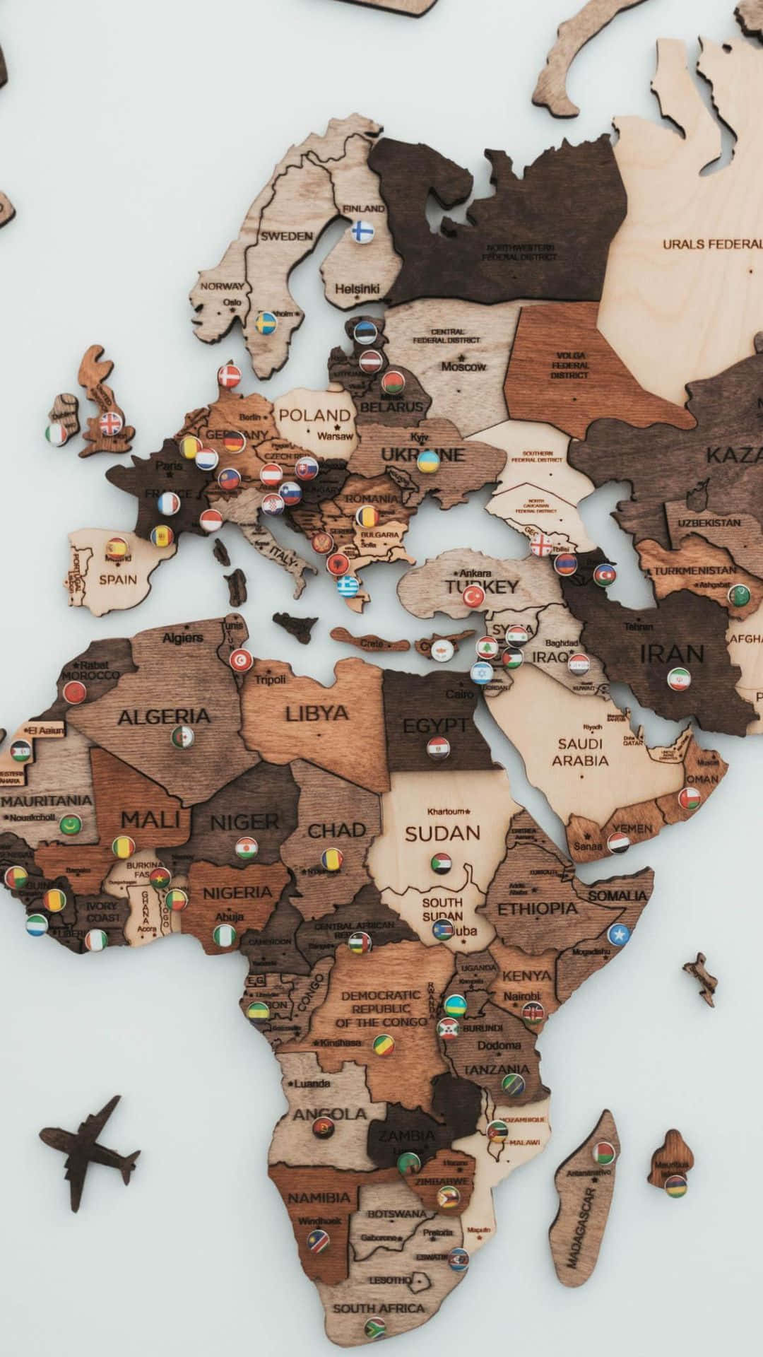 World Map Aesthetic 桌布 壁紙 — 一個木製世界地圖，上面有國家名稱和彩色圖釘標記目的地，附近有一架小飛機。