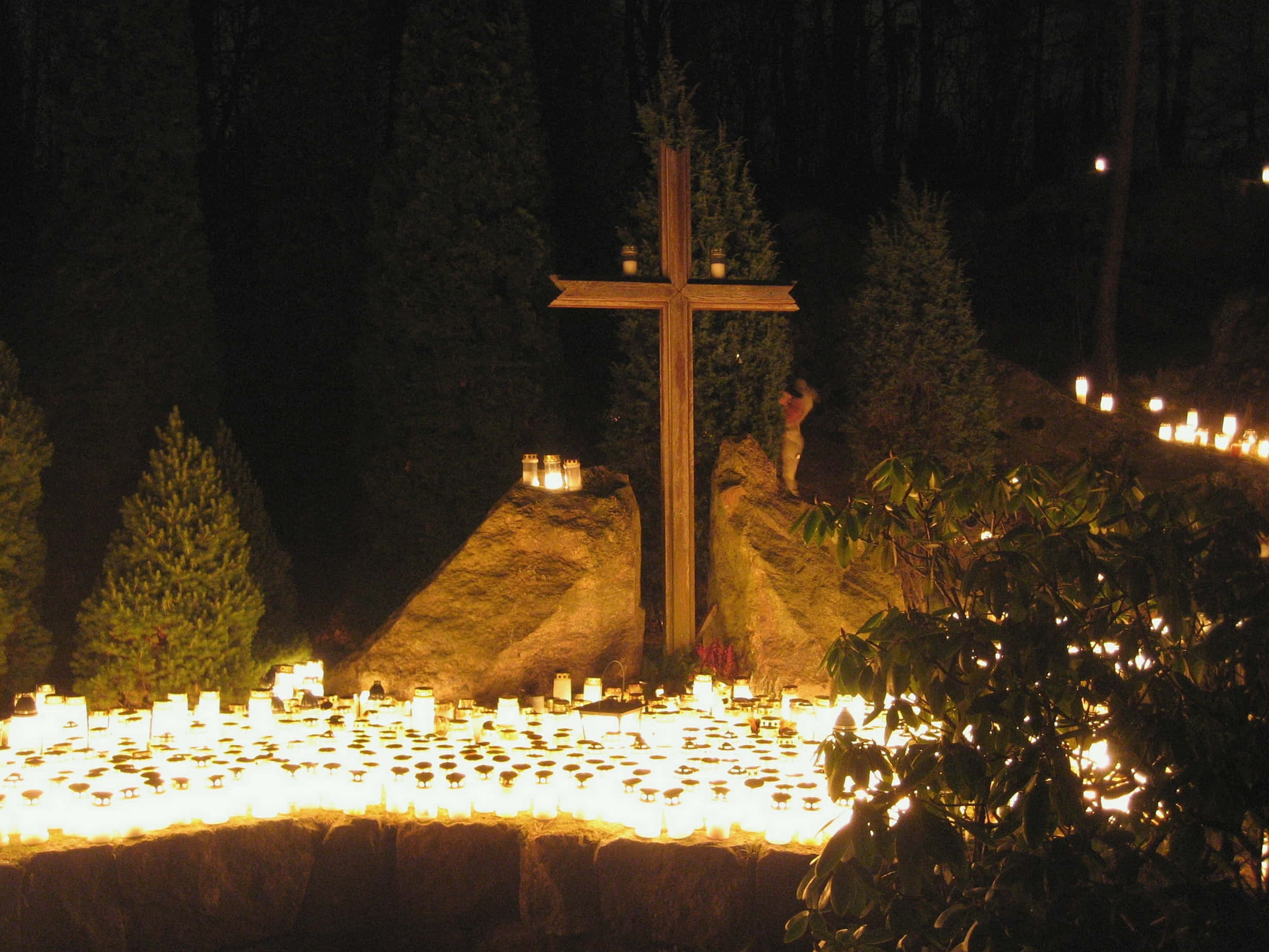 Religious Christmas 桌布 壁紙 — 一個木製十字架在夜晚的黑暗森林中，被數百支發光的蠟燭照亮。