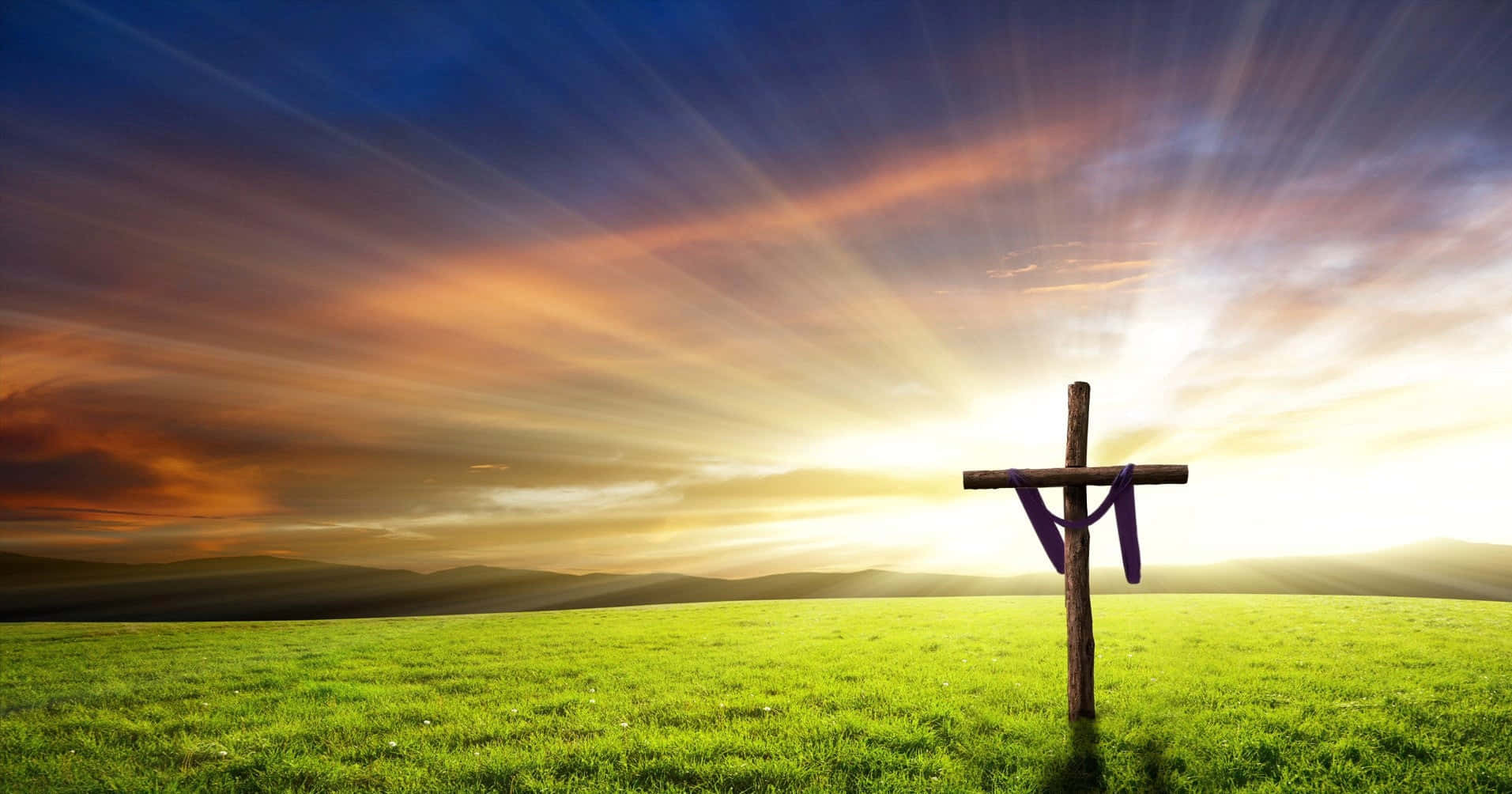 Palm Sunday 桌布 壁紙 — 一個木製十字架掛著紫色布，獨自矗立在充滿活力的綠色田野中，背景是戲劇性的日出天空和耀眼的光芒。