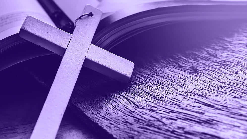 Lent 桌布 壁紙 — 一個木製十字架擱在一本打開的書上，書放在一個被紫色光照亮的風化木質表面上。