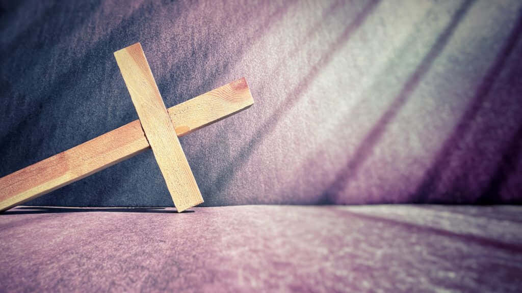 Lent 桌布 壁紙 — 一個木製十字架放置在帶有紋理的紫色表面上，戲劇性的燈光投射出對角線陰影。