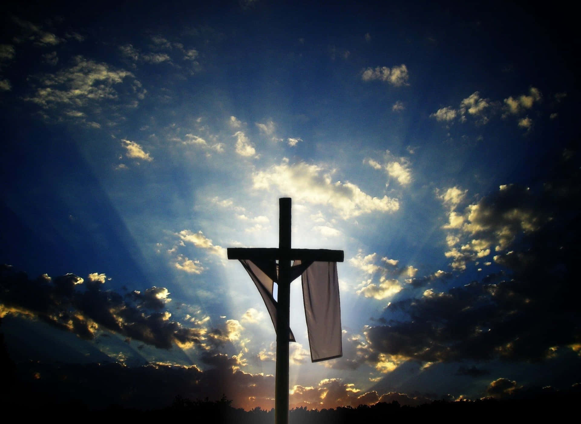 Catholic 桌布 壁紙 — 一個木製十字架的剪影，矗立在戲劇性的天空下，夕陽的金色雲層中透出耀眼的光芒。