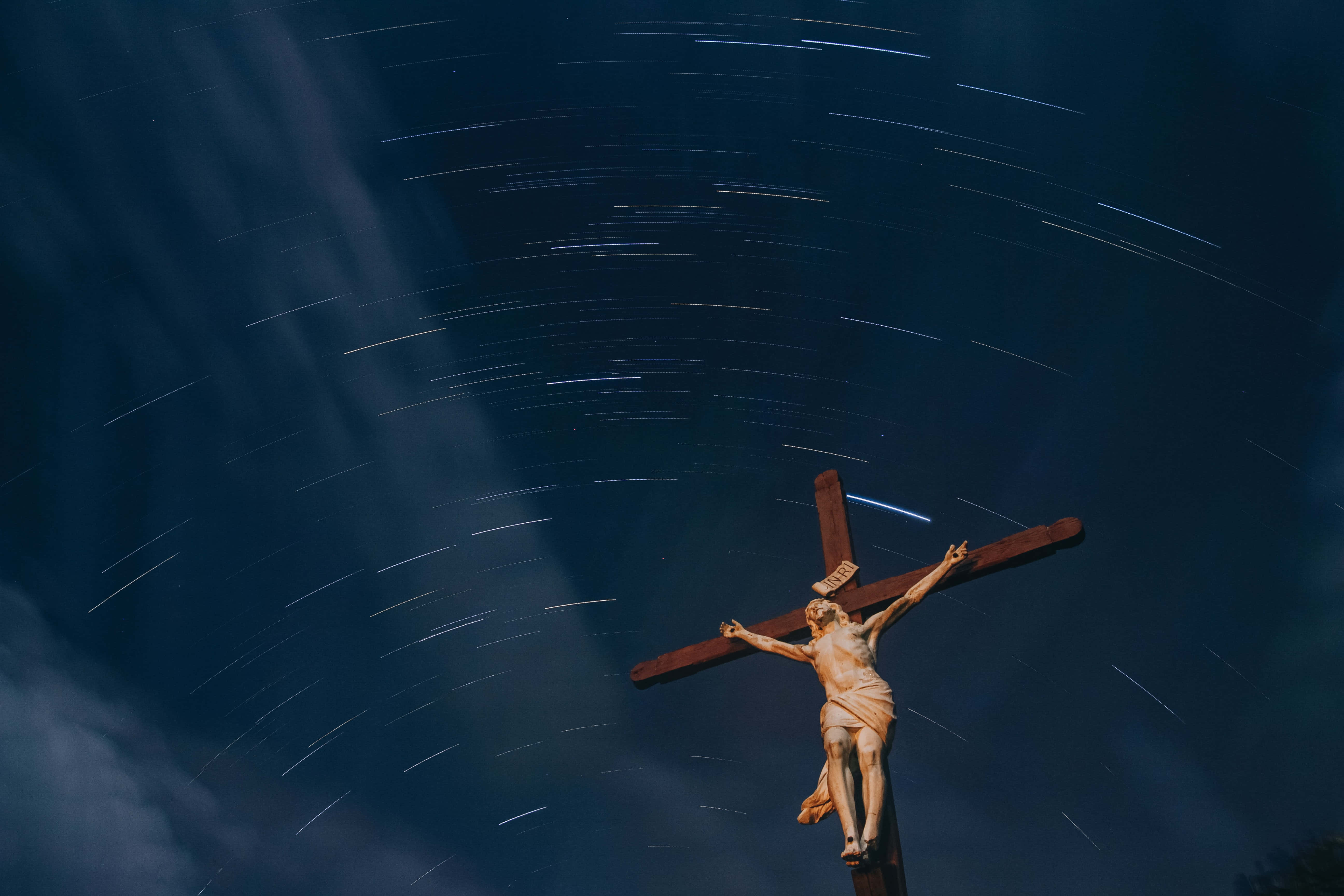 Jesus Saves 桌布 壁紙 — 一個木製十字架雕像矗立在星軌天空下，天空中有旋轉的藍色和白色光條。
