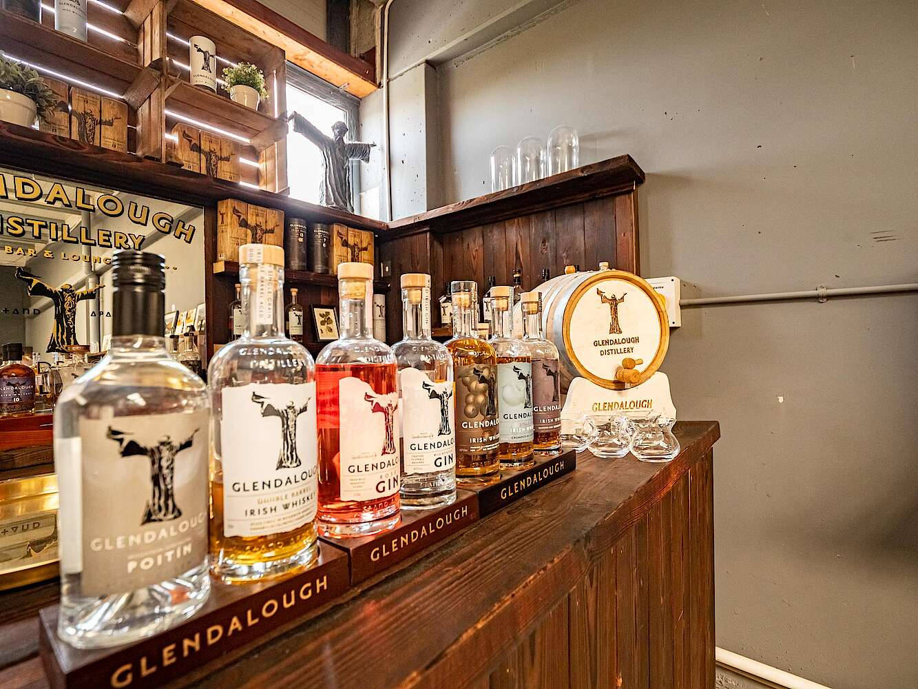 品牌 桌布 壁紙 — 一個木製吧檯展示Glendalough烈酒瓶，配有品牌酒杯和陳列商品的貨架，位於質樸的釀酒廠休息室。