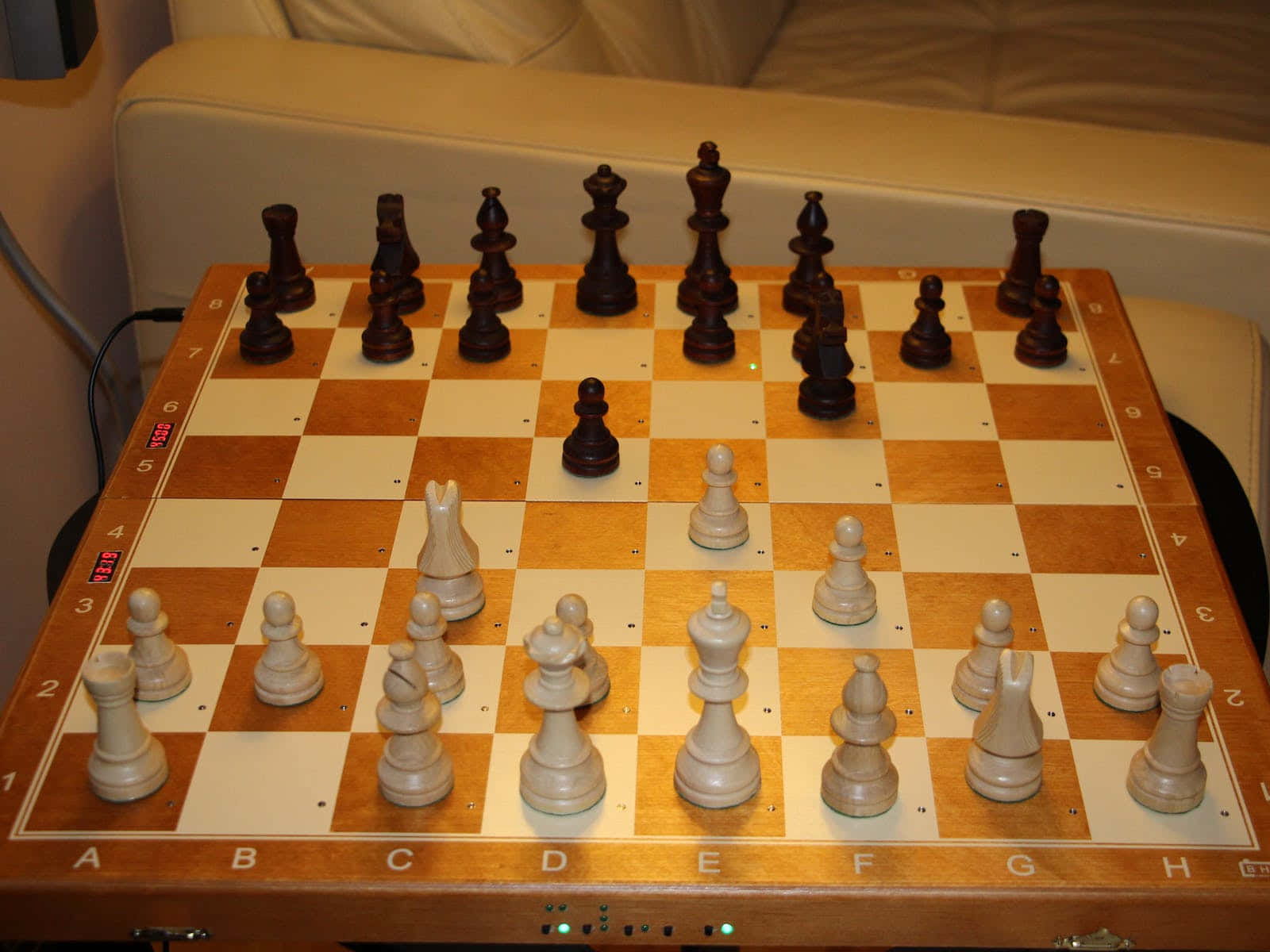 Chessboard 桌布 壁紙 — 一個木製棋盤，上面擺放著深色和淺色的棋子準備對弈，棋盤擱在米色沙發旁邊的桌子上。