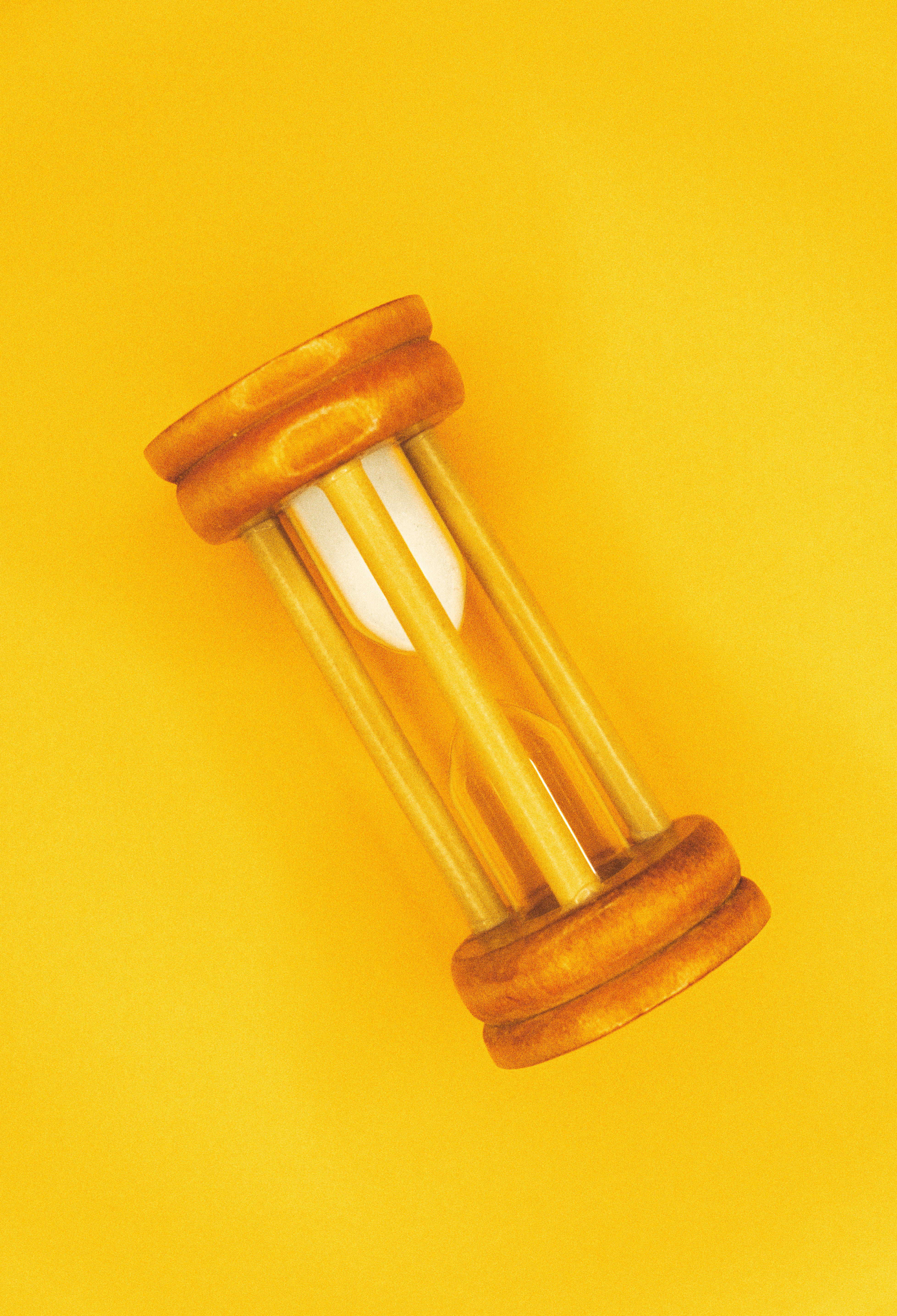Hourglass 桌布 壁紙 — 一個木製沙漏，白色沙子慢慢滴落，背景是鮮黃色。