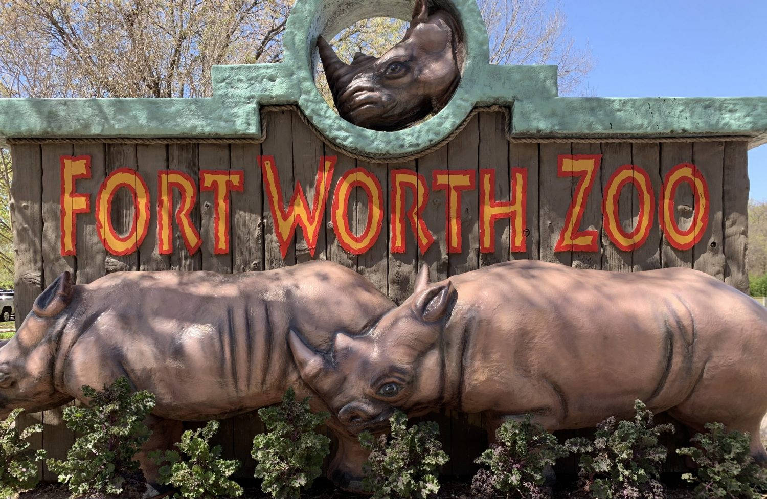 Worth 桌布 壁紙 — 一個木製的Fort Worth動物園標誌，下方有兩個犀牛雕塑和一個犀牛頭剪影，背景是晴朗的藍天。